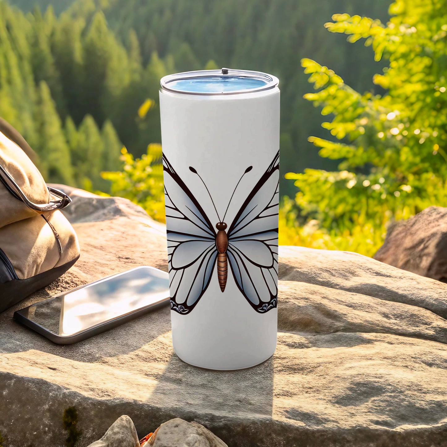 White tumbler with butterfly graphic, resting on rocks outdoors.