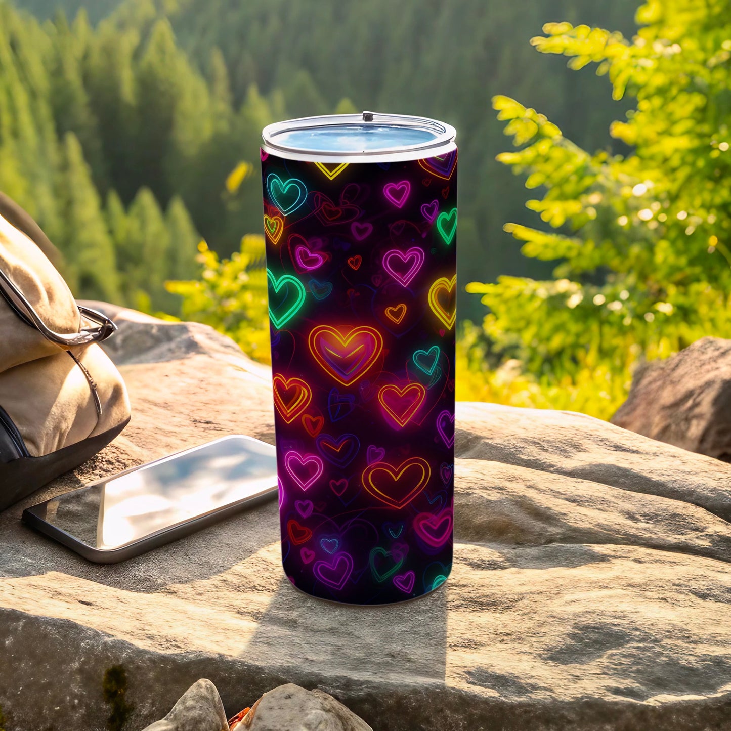 Black tumbler with neon heart pattern, on a rock outdoors.