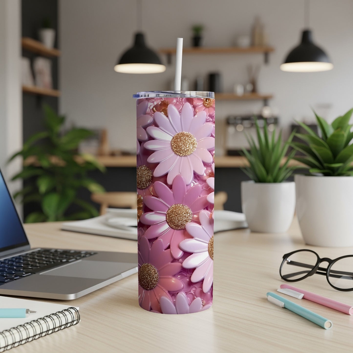 Pink floral tumbler with straw on a desk with laptop and pens.
