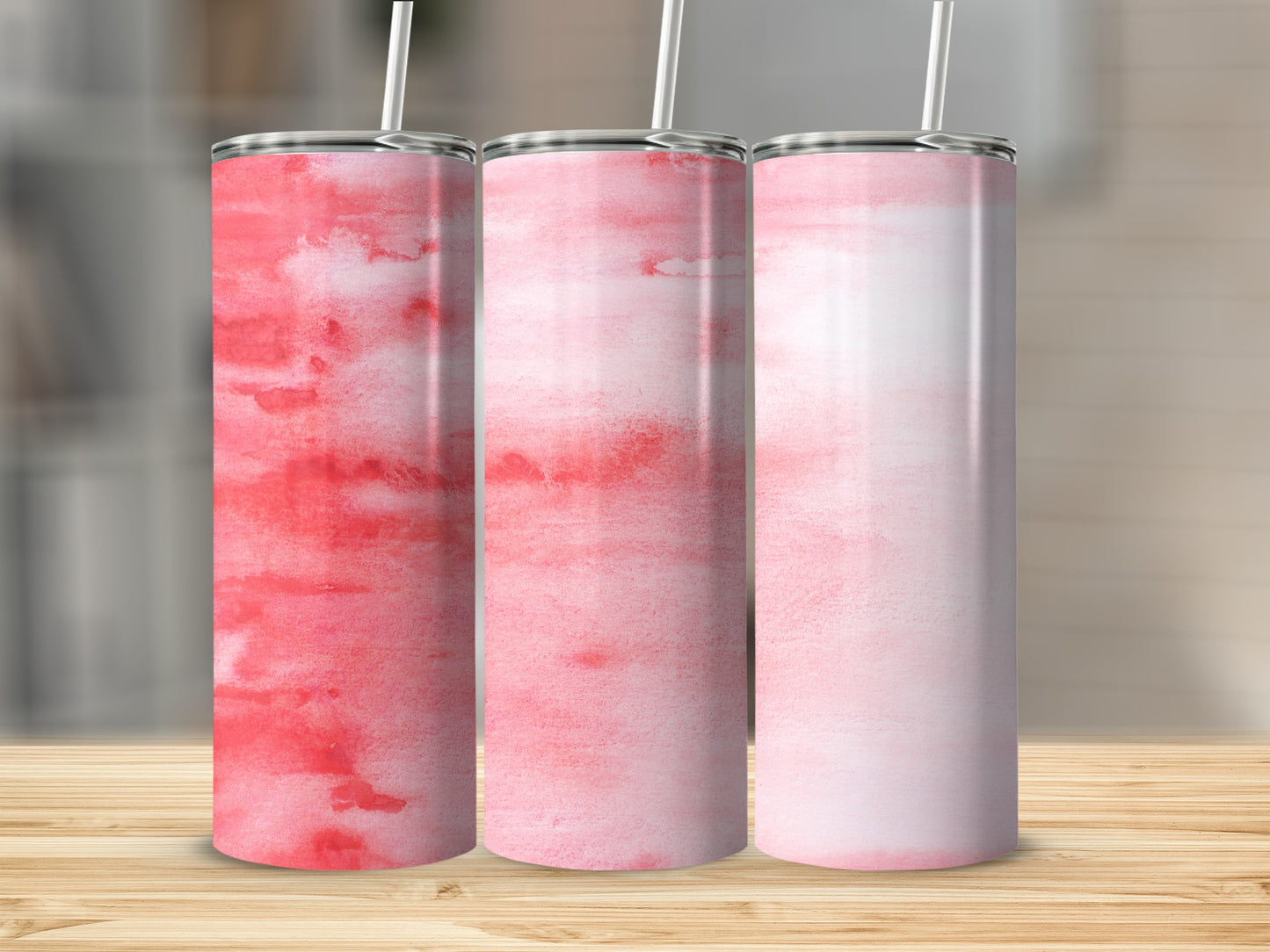 Three pink watercolor tumblers with straws on a wooden surface.