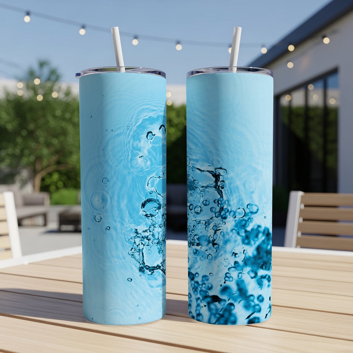 Two tall, light blue tumblers with water splash graphics and straws on a table.
