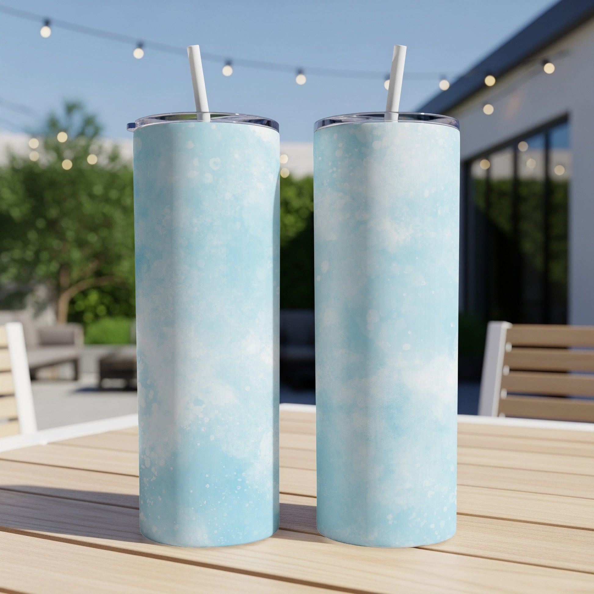 Two blue marbled tumblers with straws sit on a wooden table outdoors.