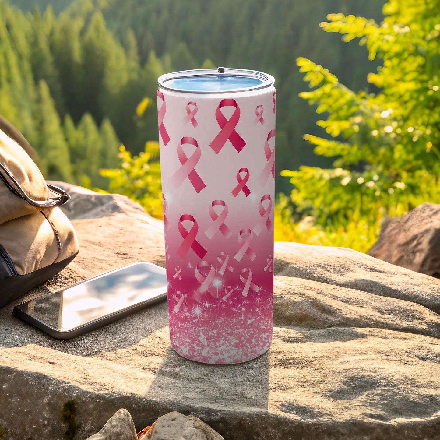 Pink ribbon pattern tumbler with sparkly accents on rocks outdoors.
