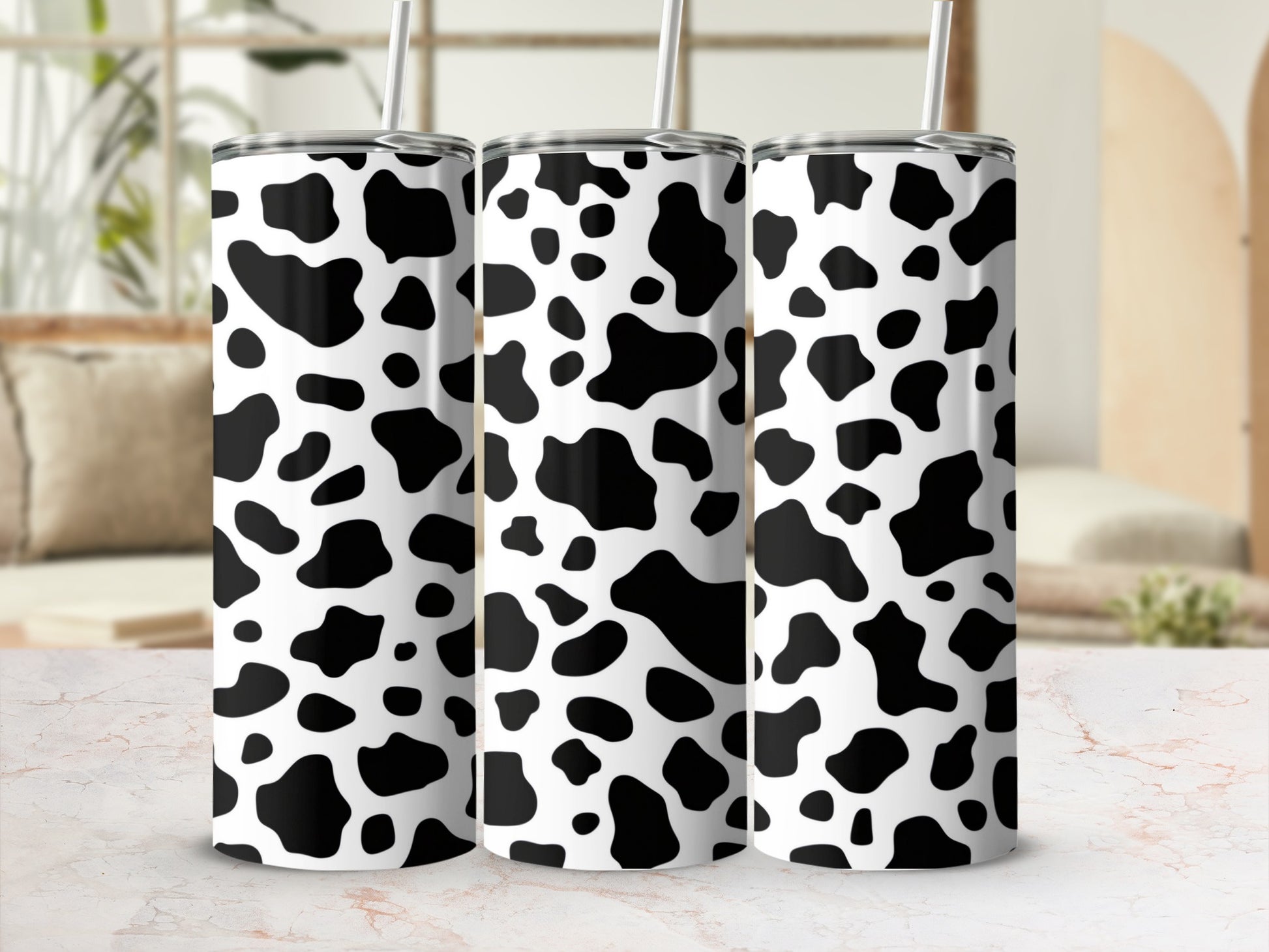 Three white tumblers with black cow print pattern and straws.