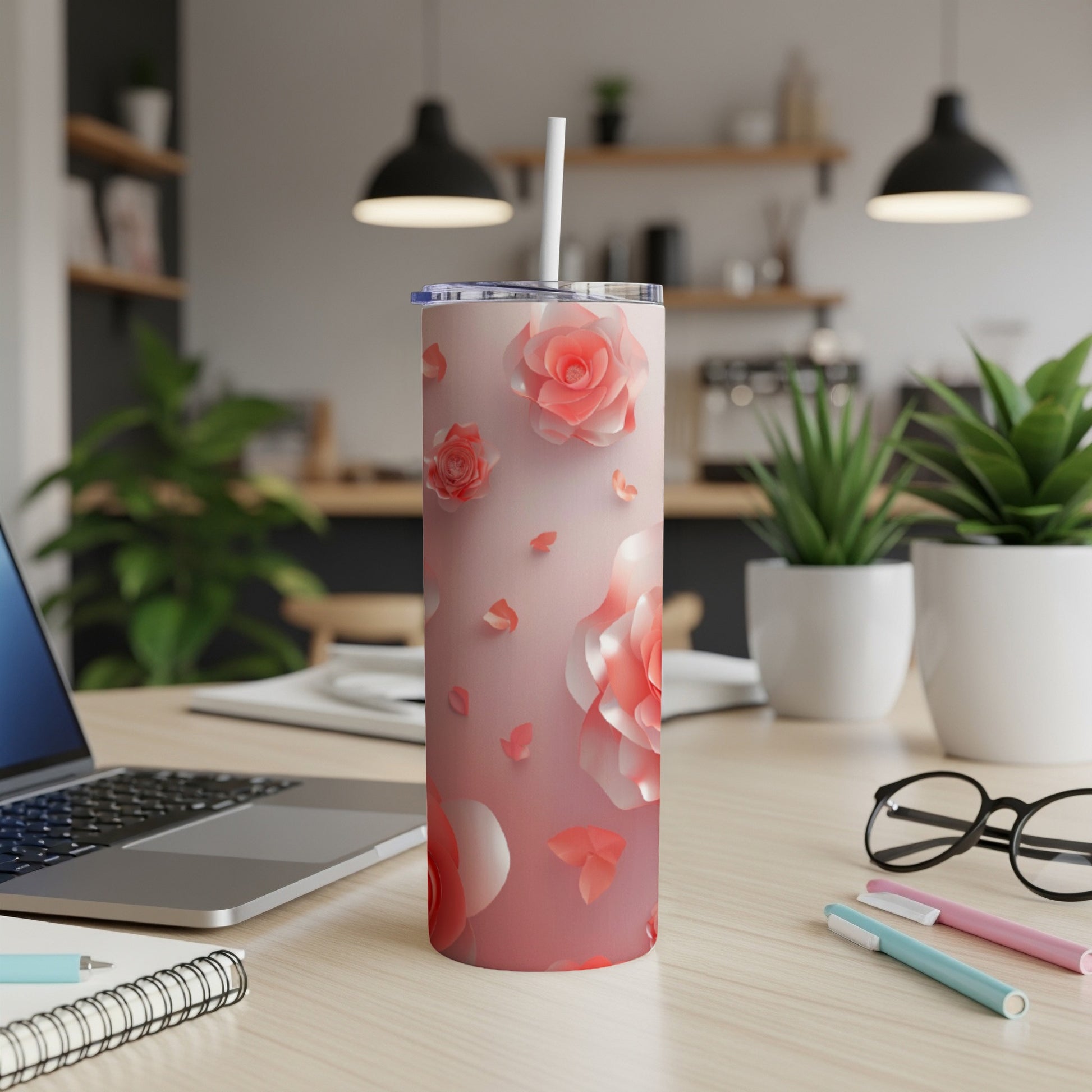 Pink floral pattern tumbler with straw on desk, next to laptop and pens.