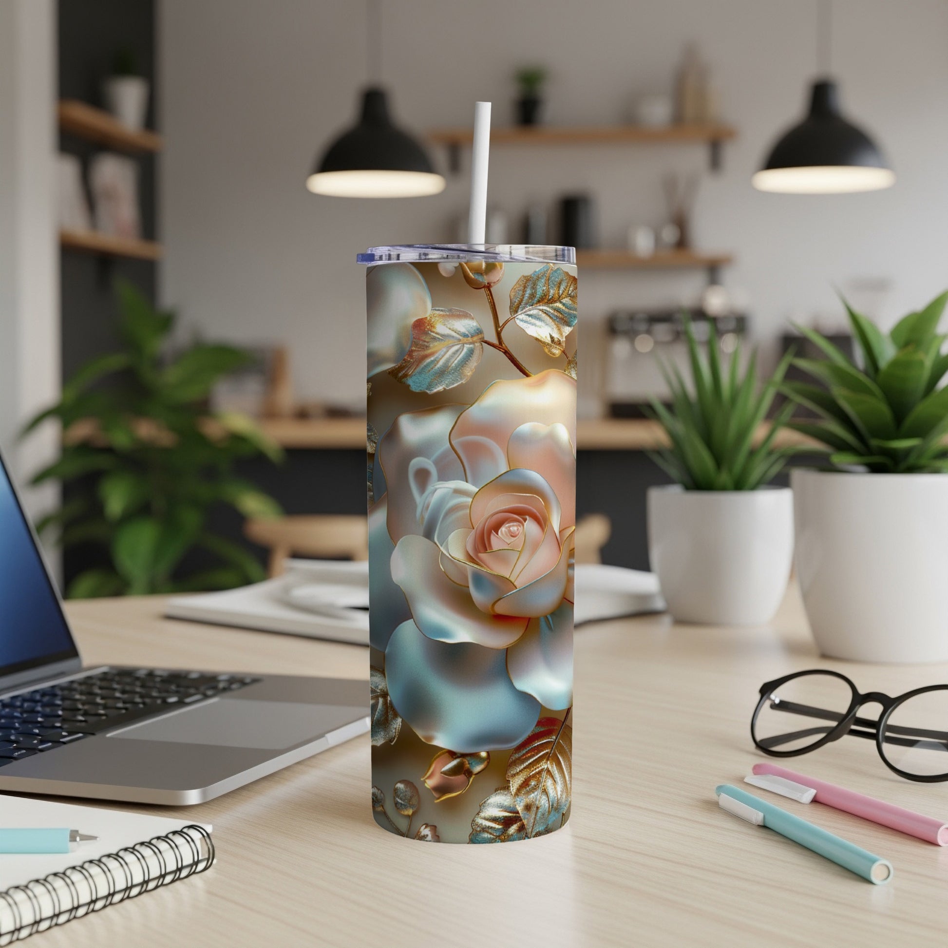 Floral rose tumbler with straw on desk next to laptop and pens.