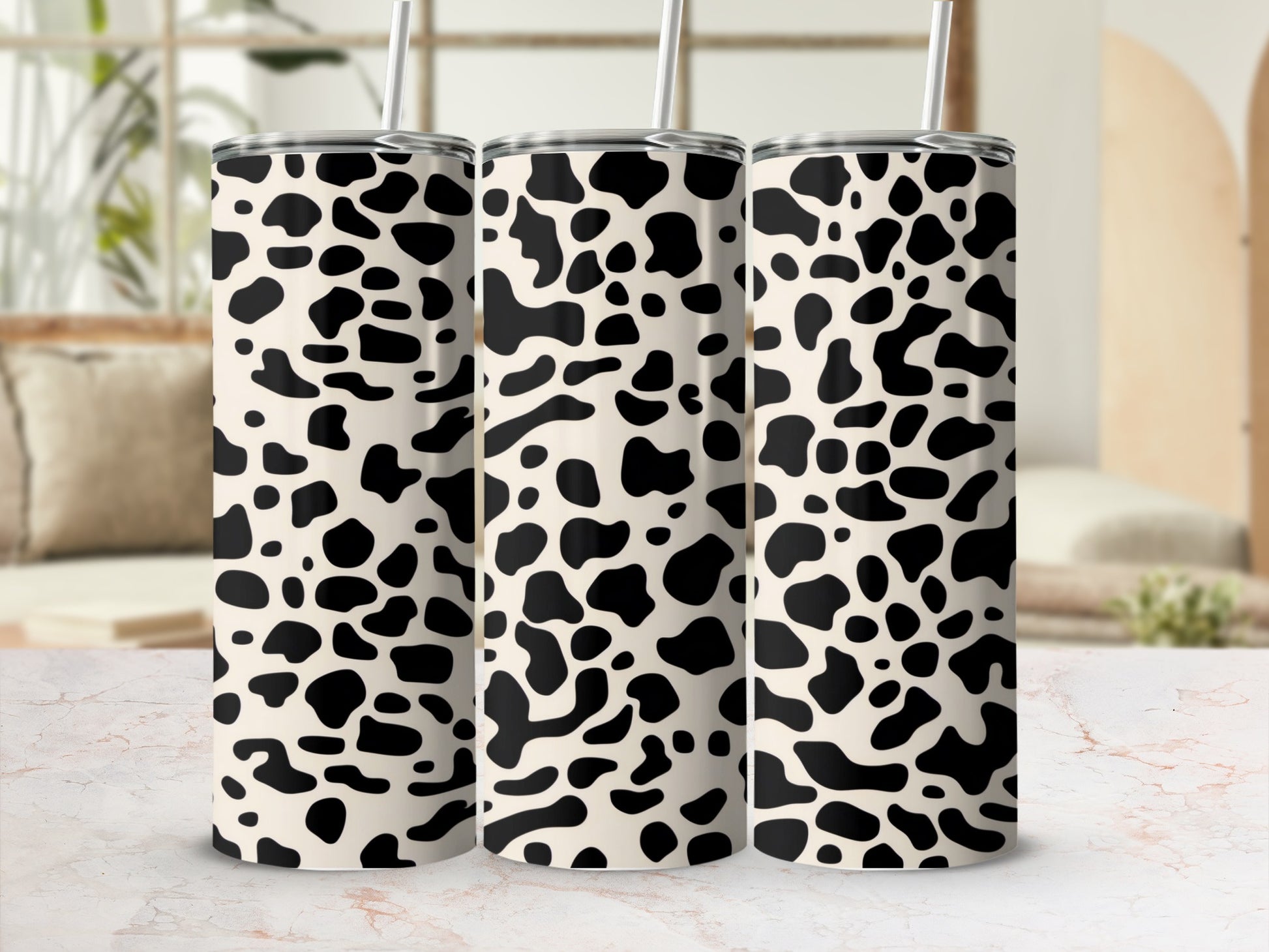 Three cow print tumblers with straws on a marble surface.