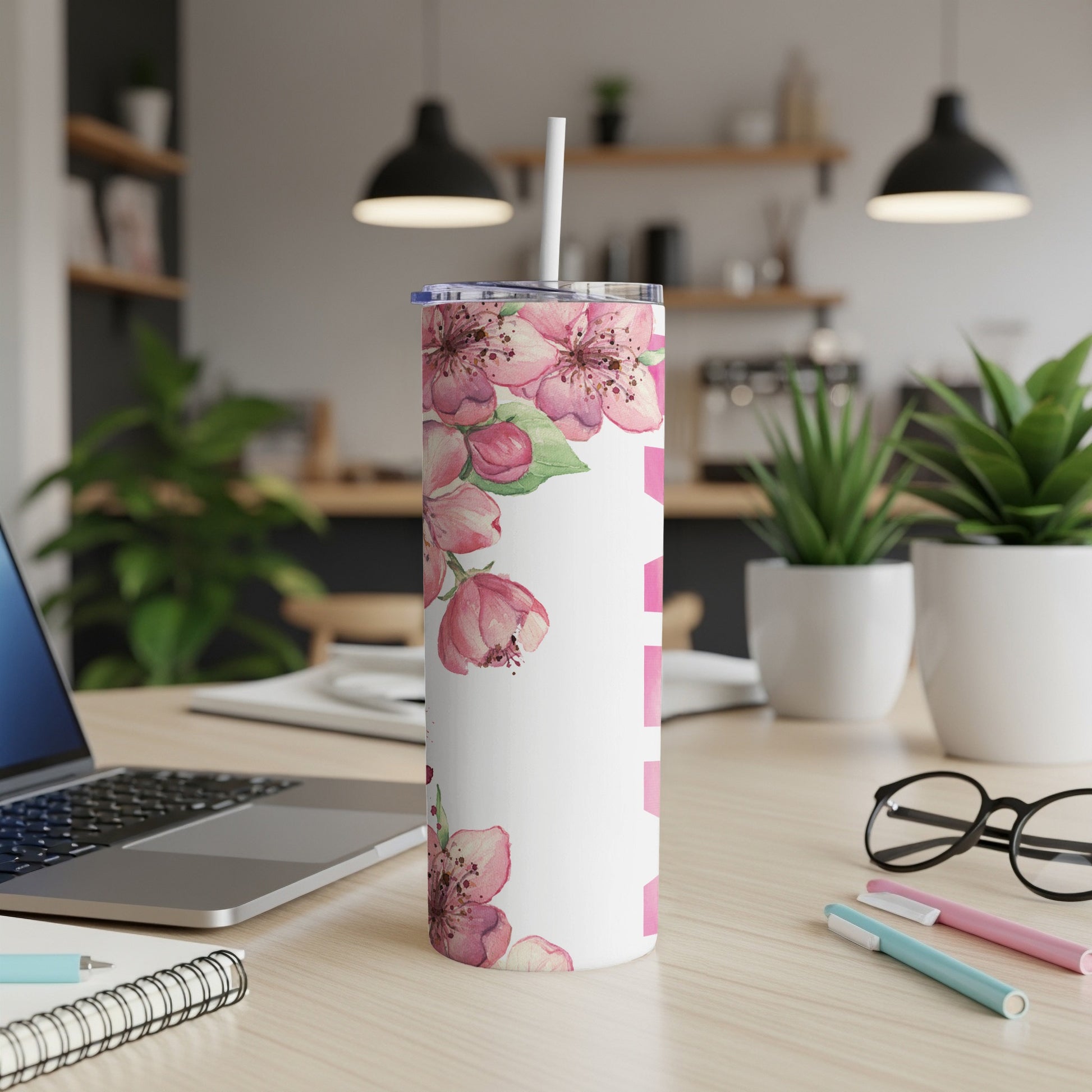 White tumbler with pink floral pattern on desk with laptop and pens.