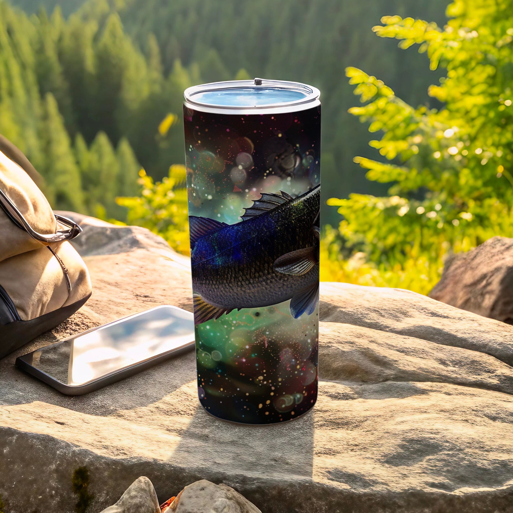 Tumbler with a large fish and cosmic background, on a rock outdoors.