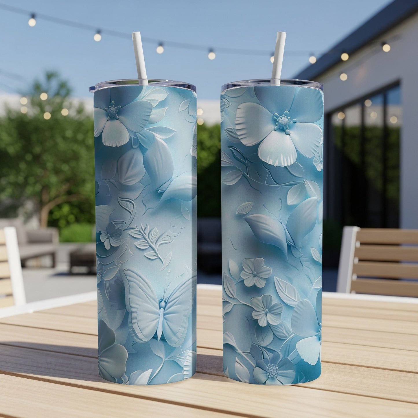 Two light blue floral pattern tumblers with butterflies on a wooden table outdoors.