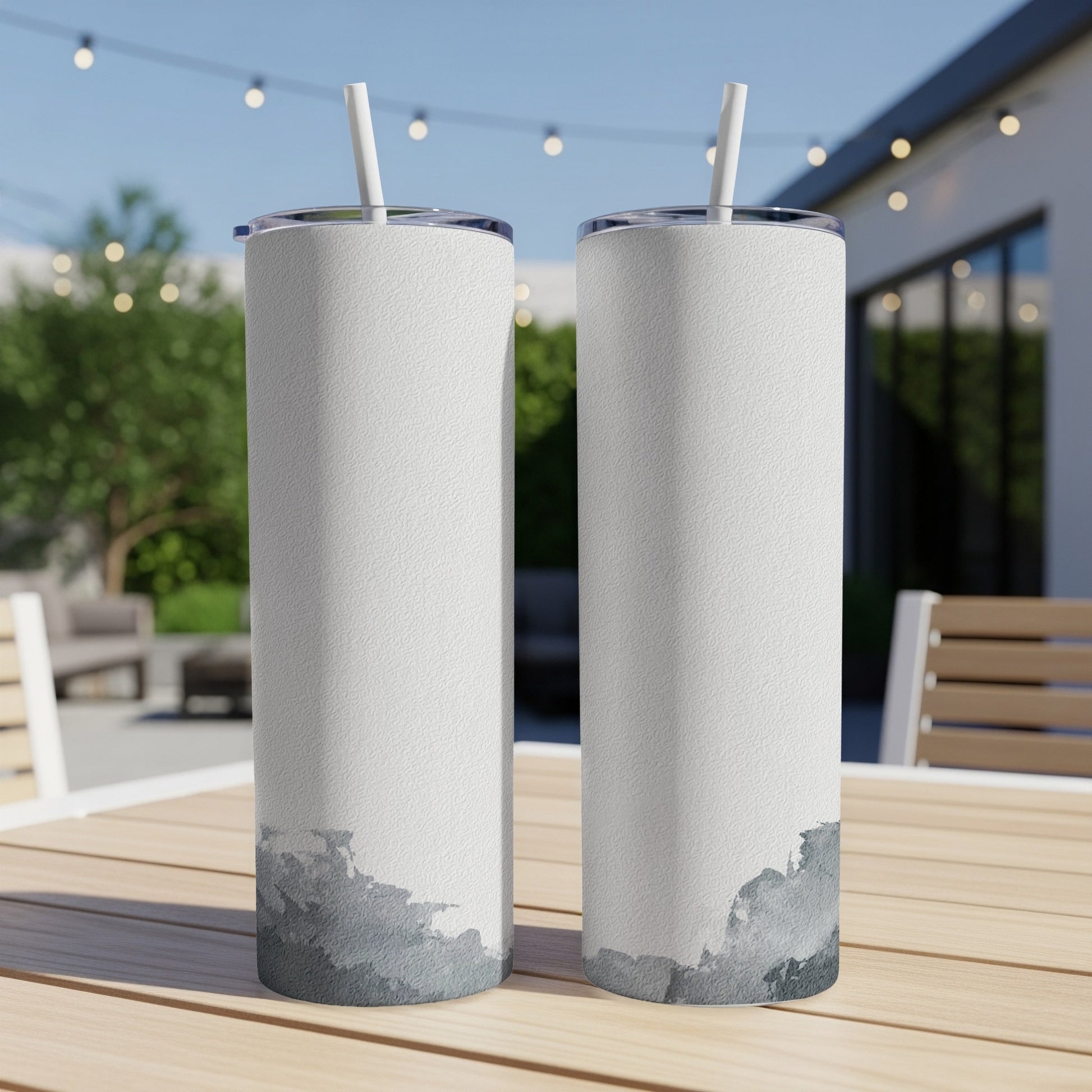 Two white tumblers with watercolor gray abstract designs sit on a wooden table.