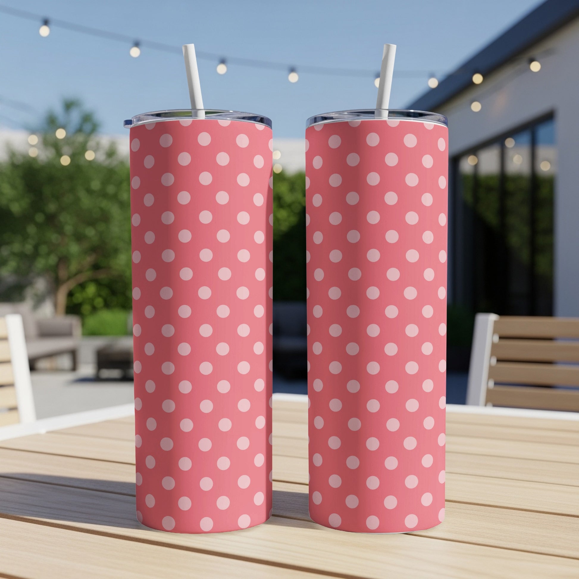 Two coral polka dot tumblers with white straws on a wooden table outdoors.