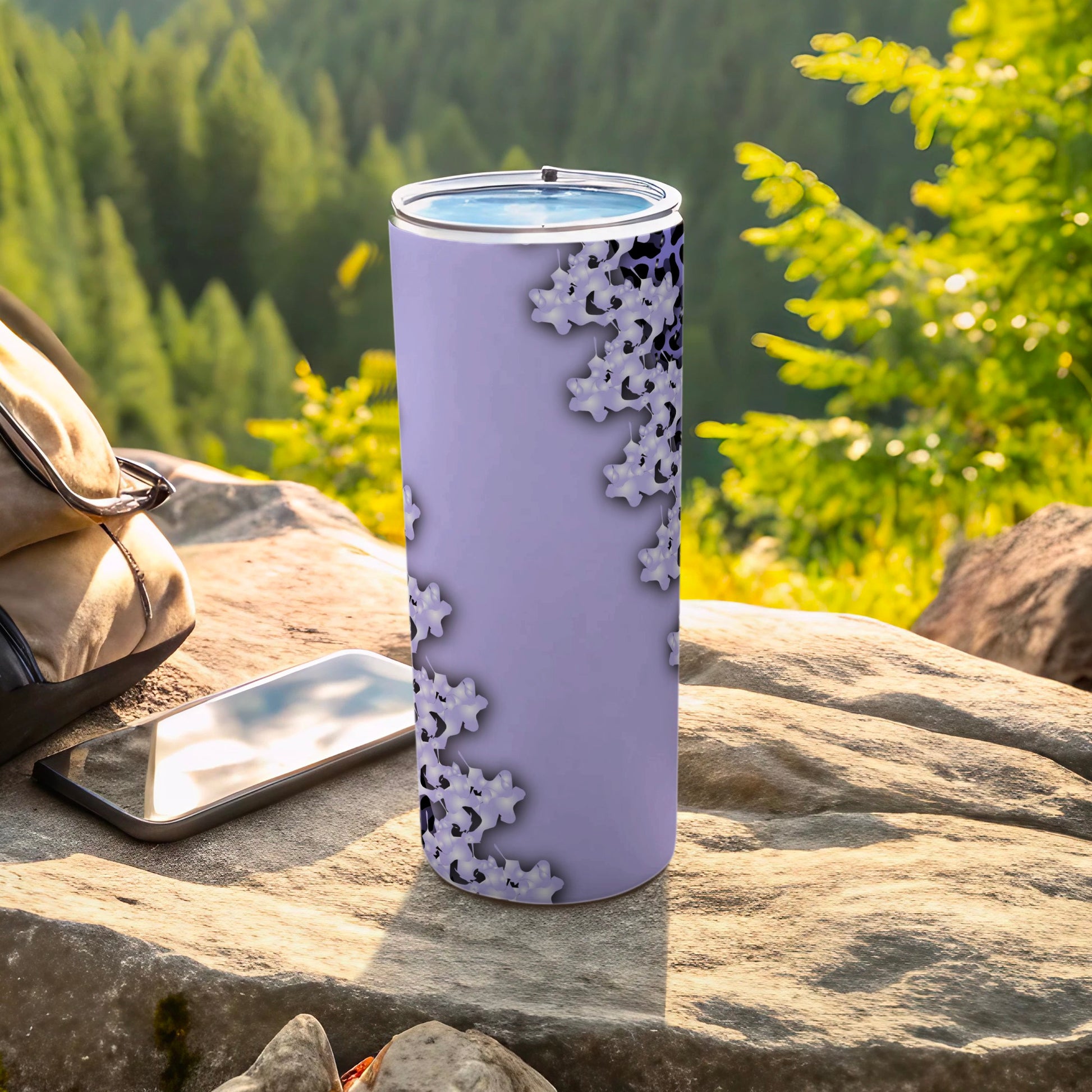 Purple tumbler with floral pattern, phone, and backpack on rocks.