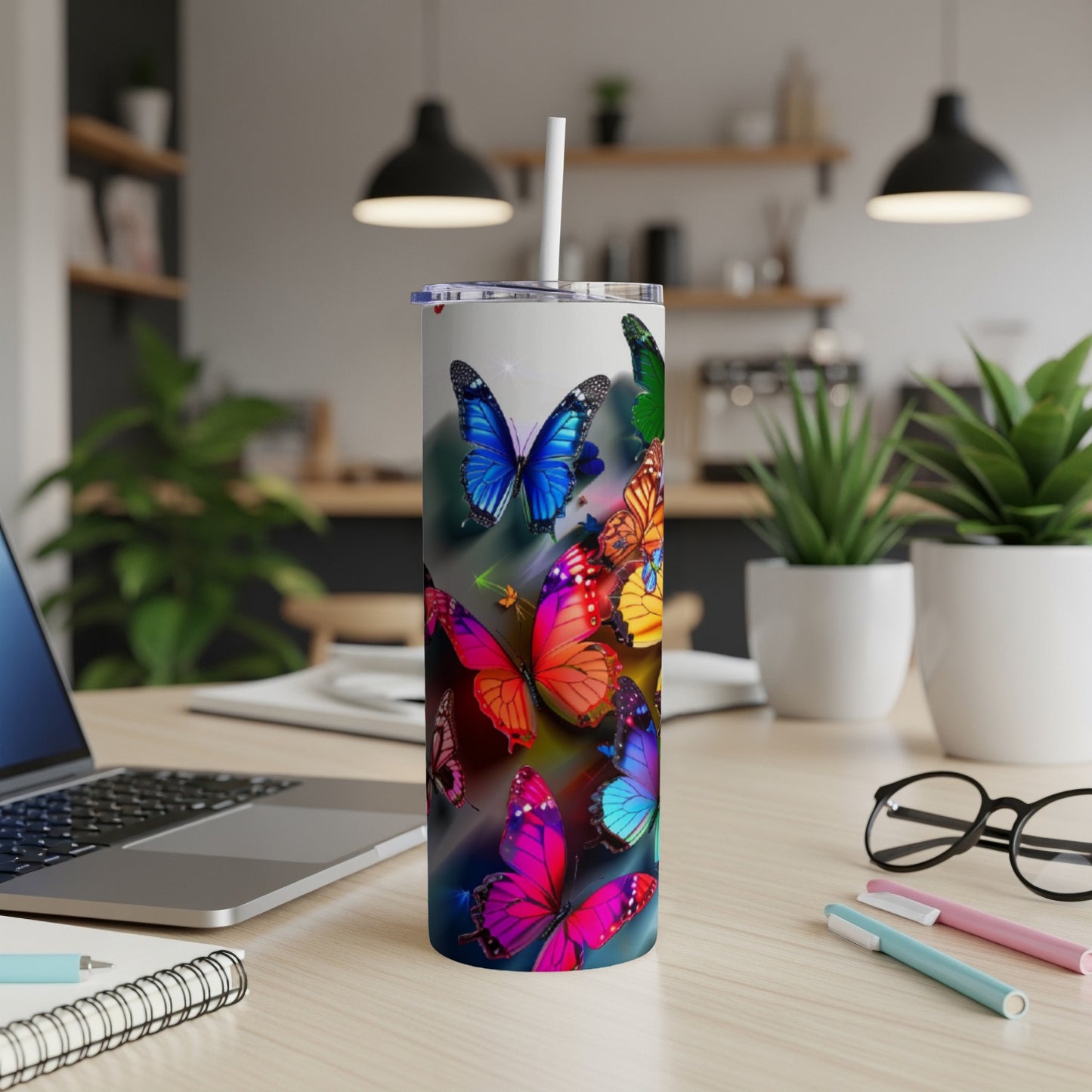 Colorful butterflies cover a white tumbler on a desk with a laptop.
