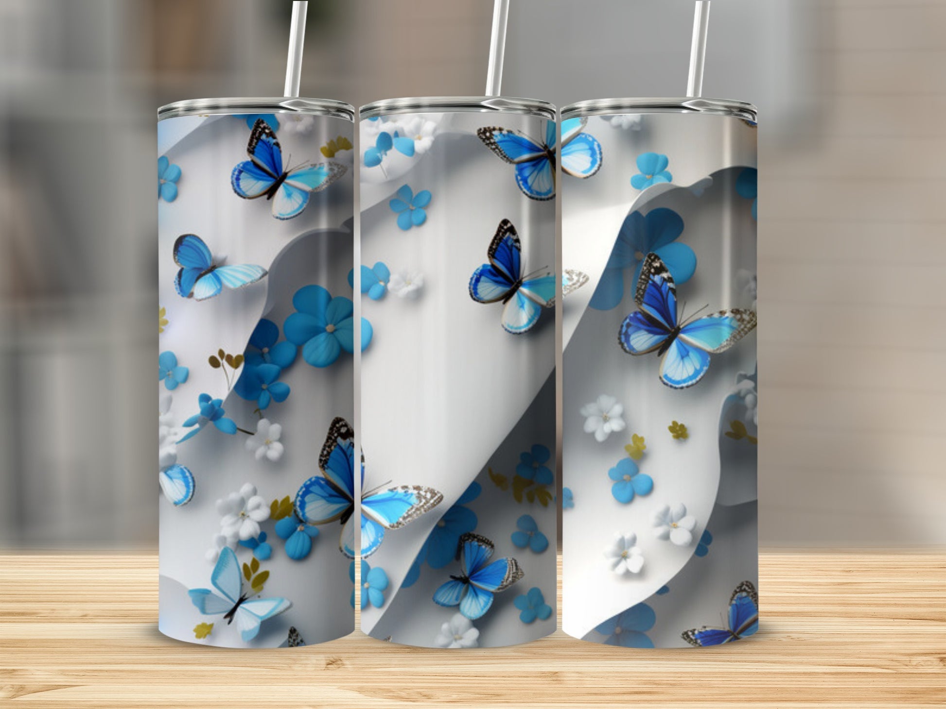 Three tumblers with blue butterflies and floral patterns on a wooden surface.