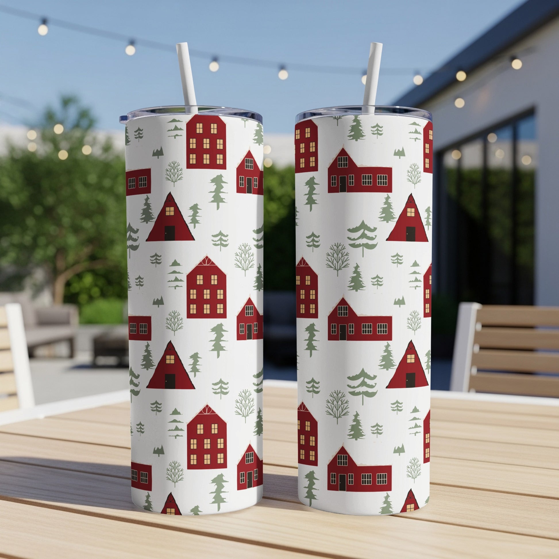 Two patterned tumblers with red houses and evergreen trees on a table.