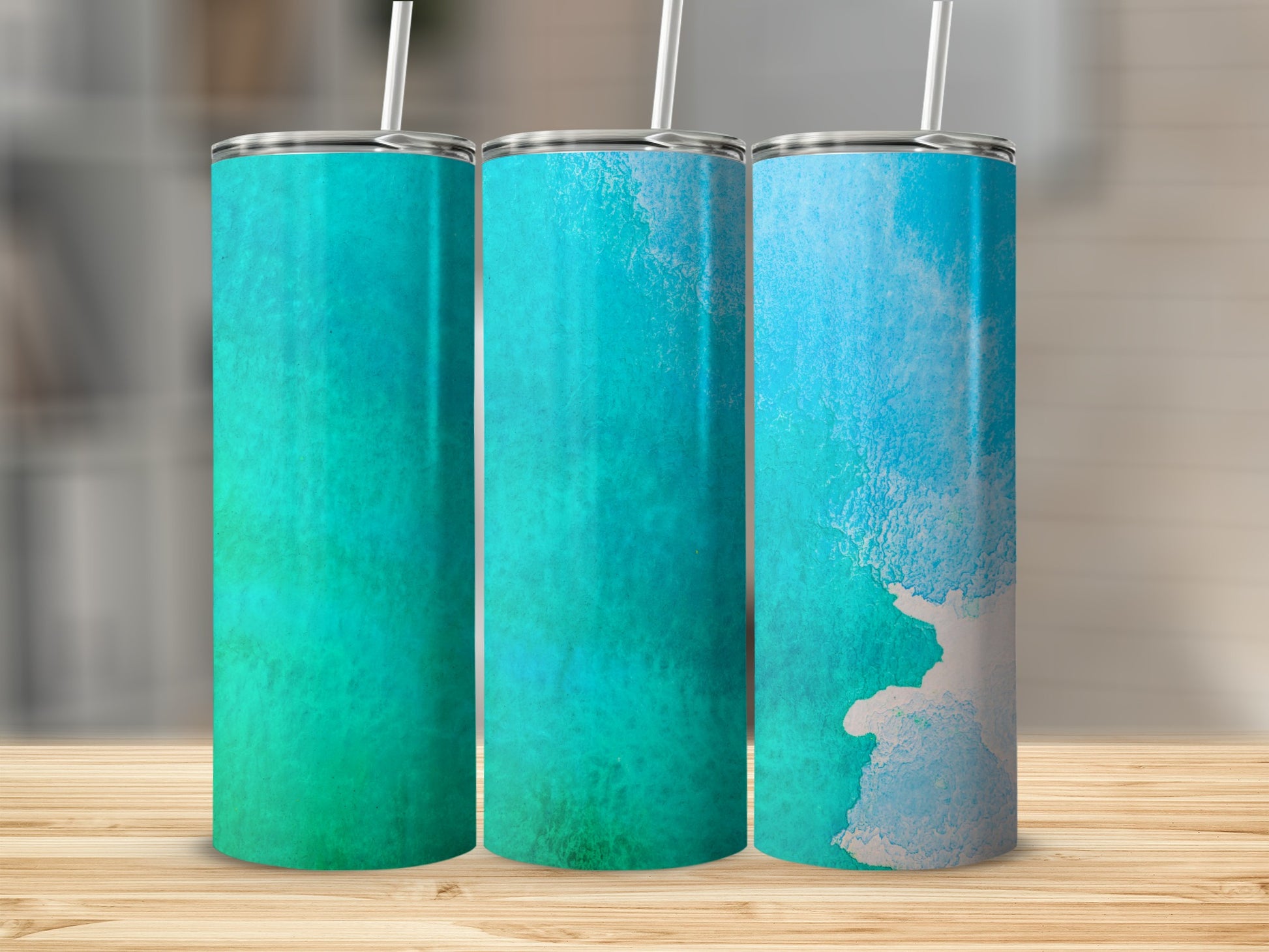 Three tumblers with watercolor designs in teal and blue on a wooden surface.