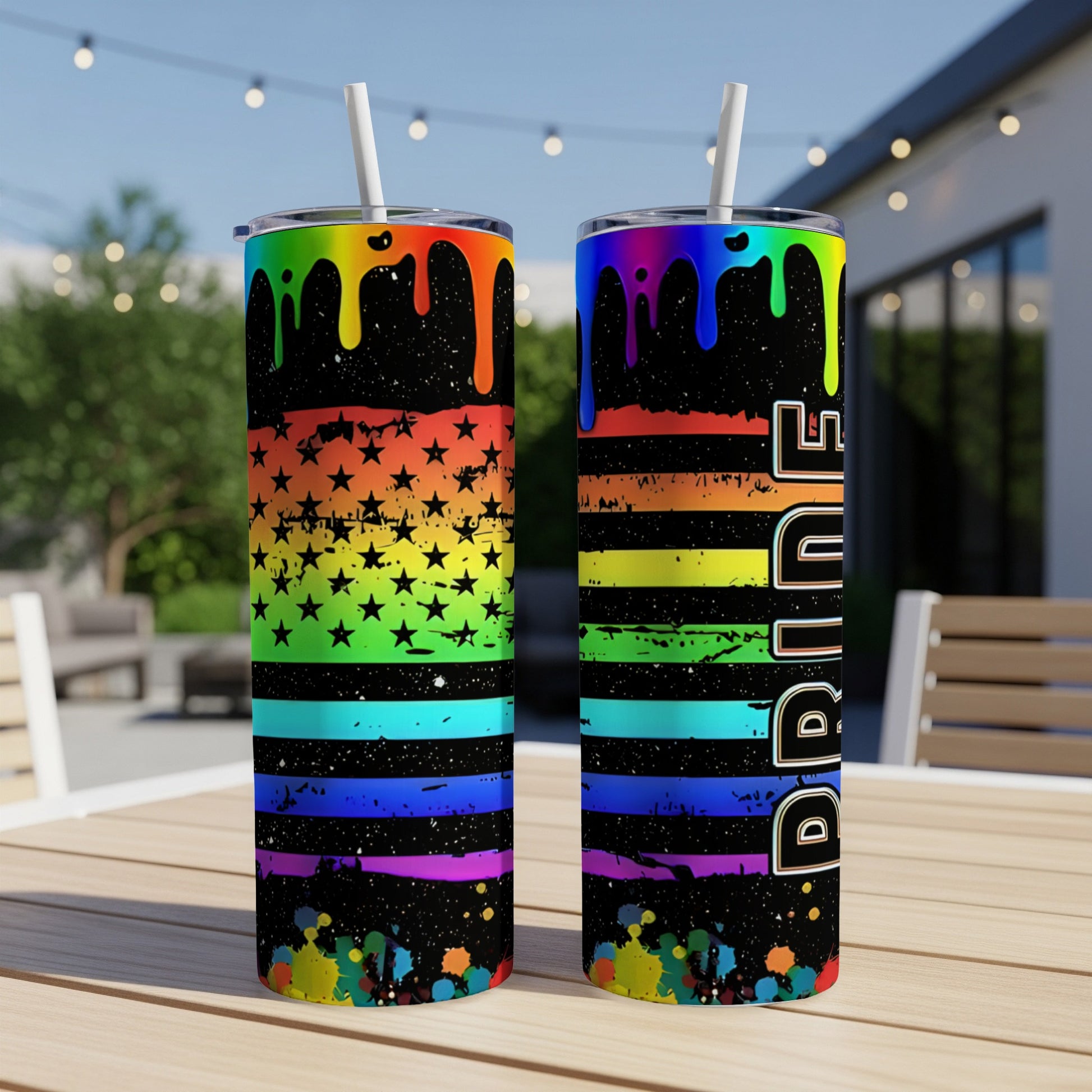Two tumblers with rainbow and flag designs sit on a wooden table outdoors.