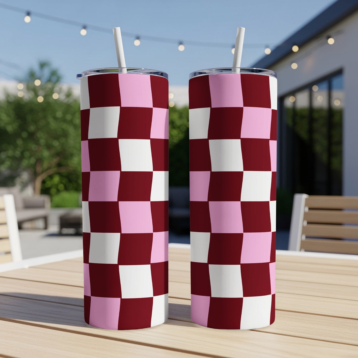 Two pink and burgundy checkered tumblers with straws on a wooden table.