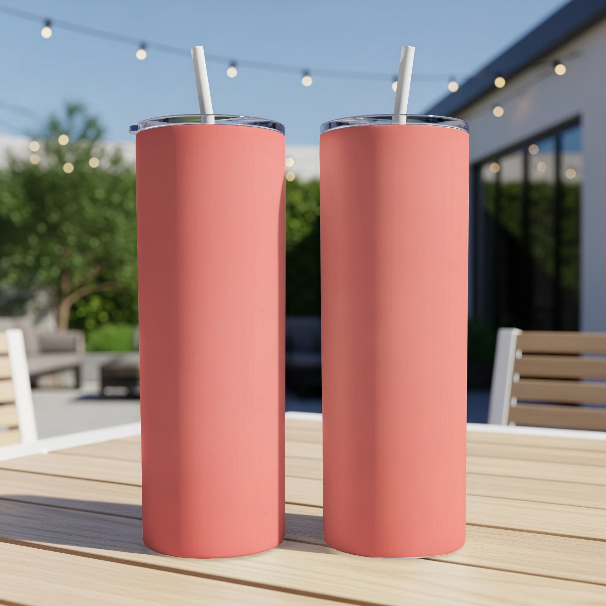 Two coral colored tumblers with white straws on a wooden table.