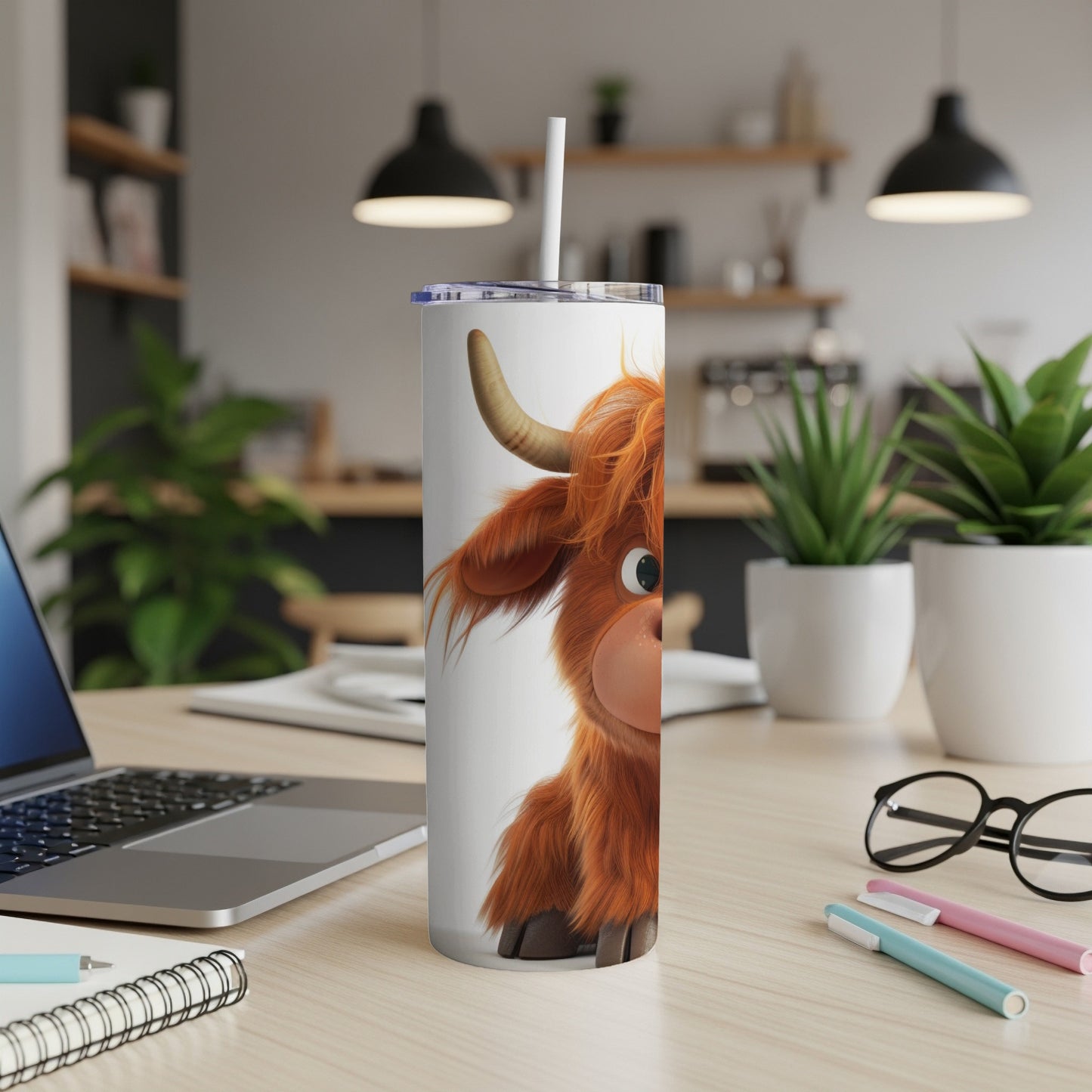 Cartoon Highland cow tumbler with straw on desk with laptop.