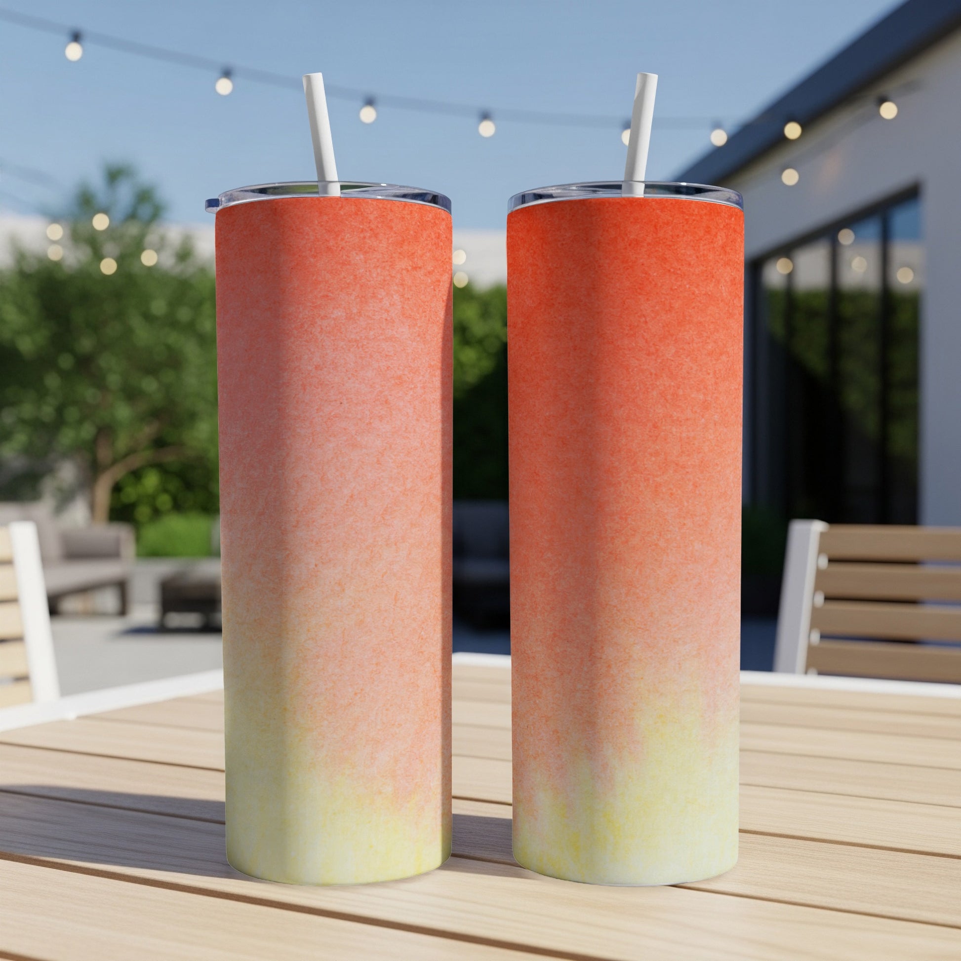 Two tall tumblers with a sunset gradient design sit on a wooden table.