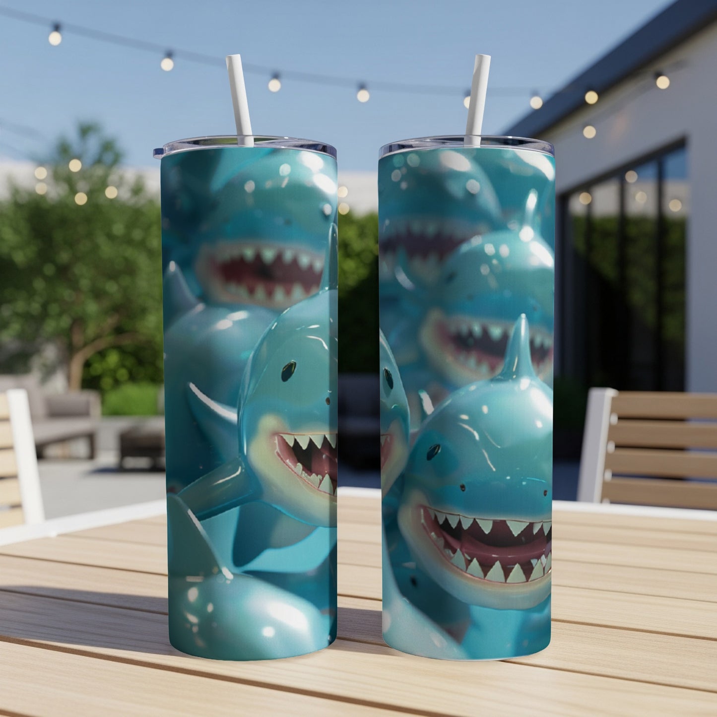 Two blue shark-themed tumblers with straws on a wooden table outdoors.