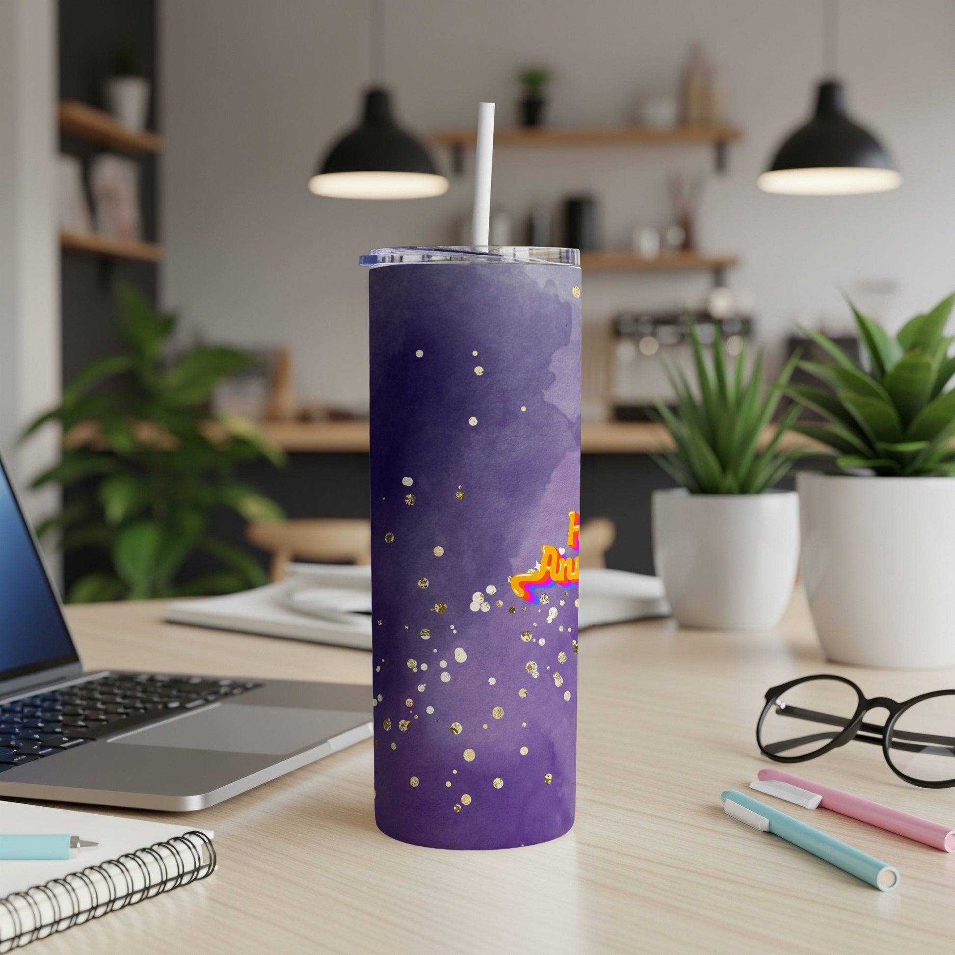 Purple tumbler with gold glitter and "Happy Birthday" text on desk.