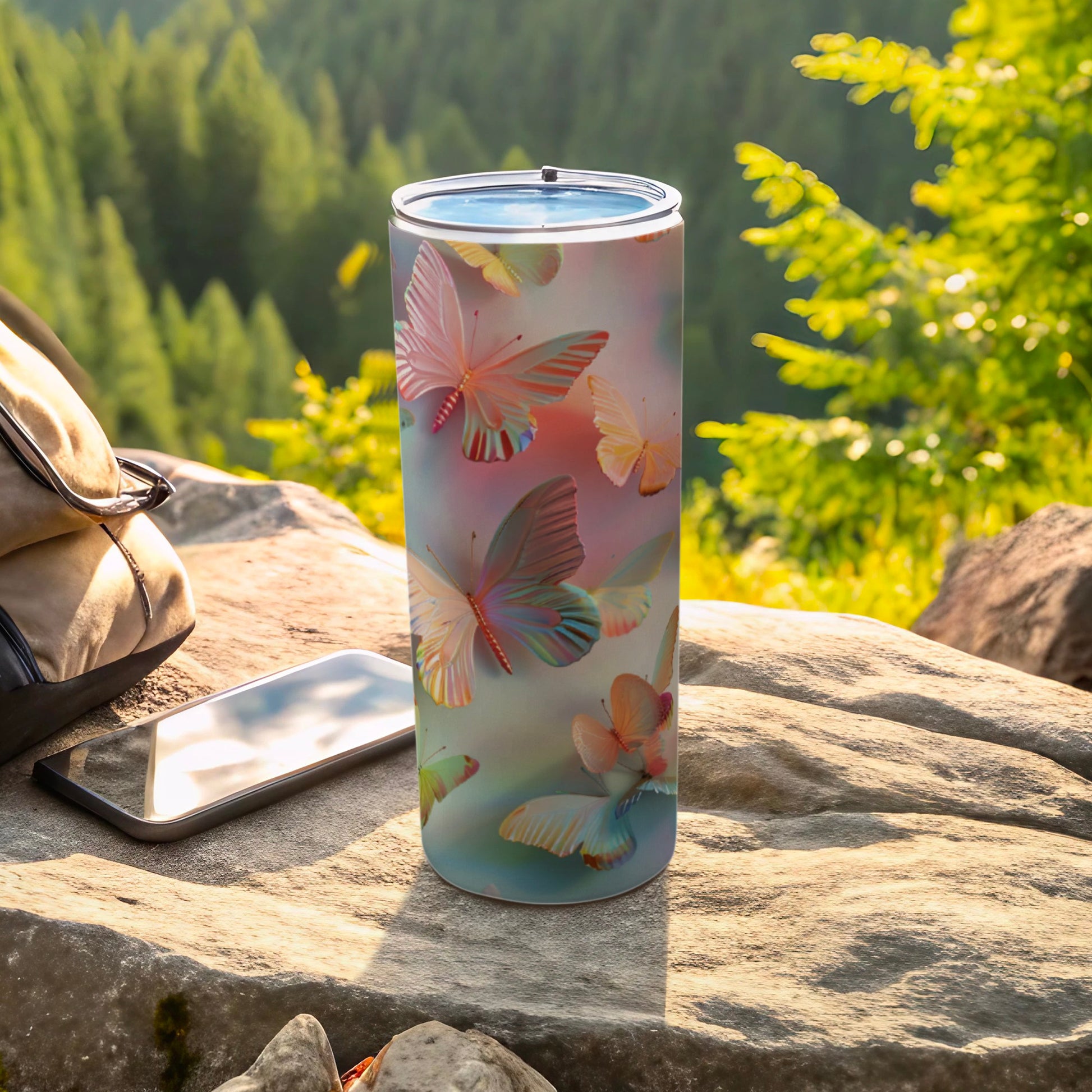 Tumbler with pastel butterflies on a rocky surface, outdoors.