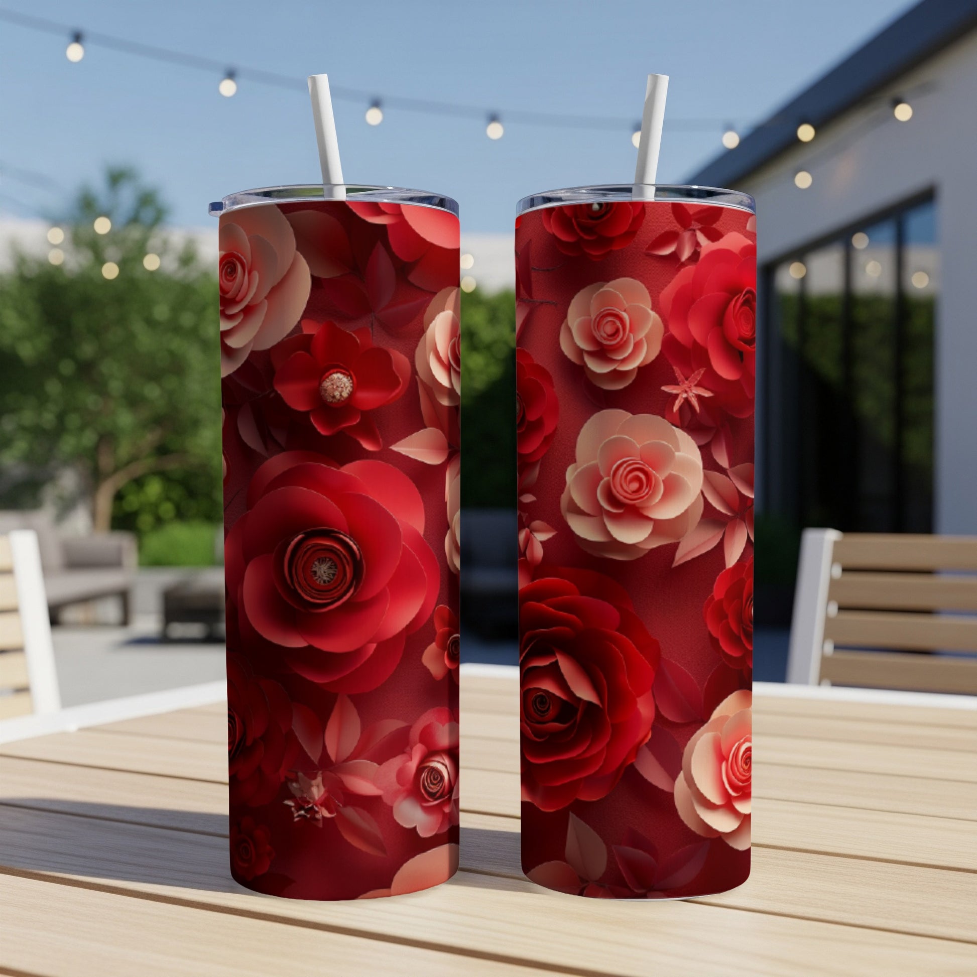 Two red floral tumblers with straws on a wooden table outdoors.