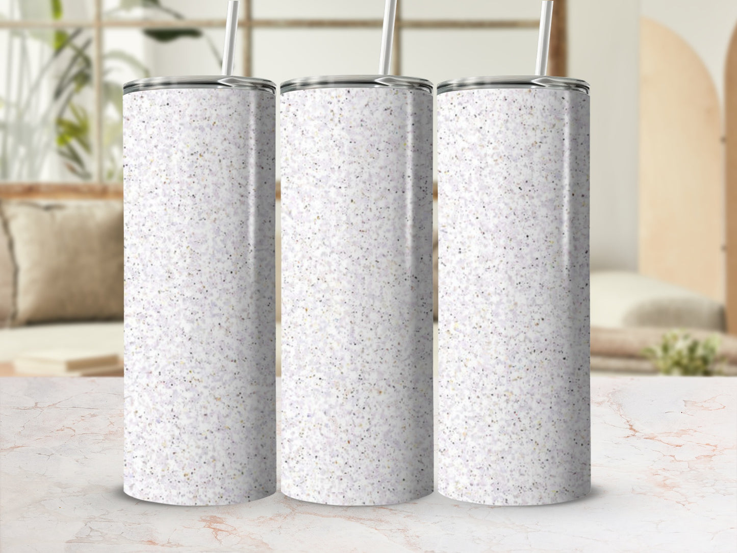 Three speckled glitter tumblers with straws on a marble surface.