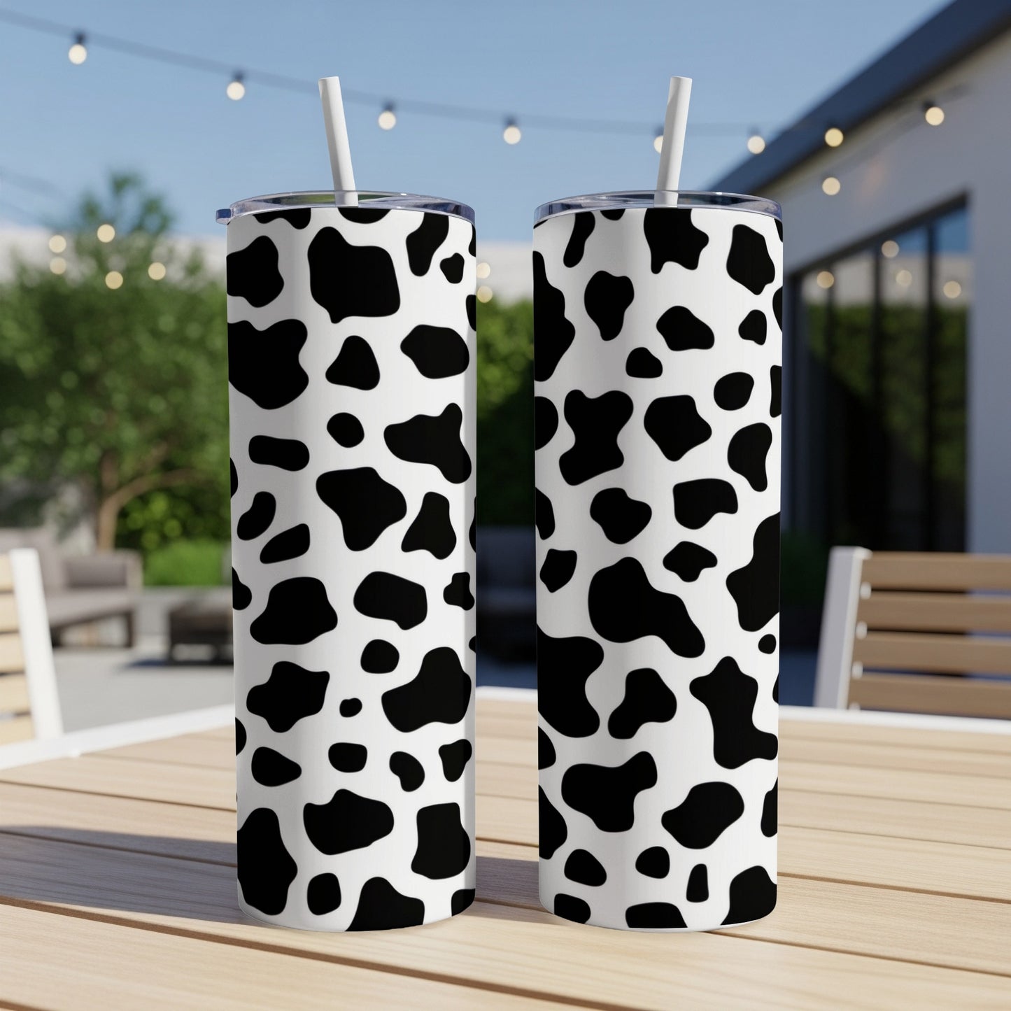 Two cow print tumblers with white lids and straws on a wooden table.