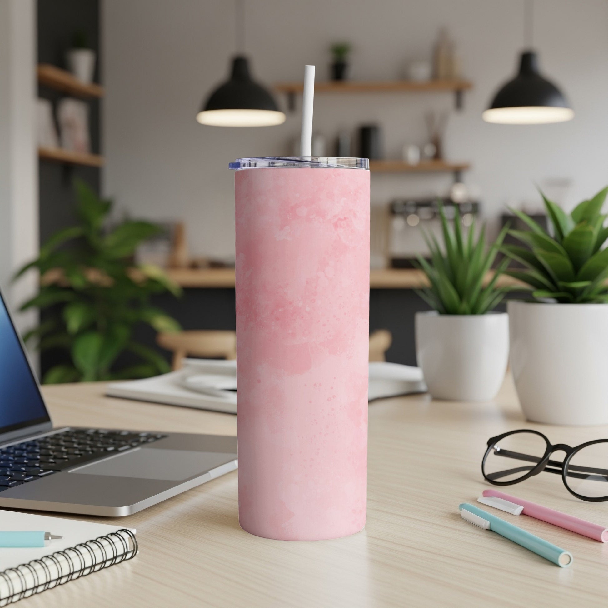 Pink marbled tumbler with straw on a desk next to a laptop and pens.