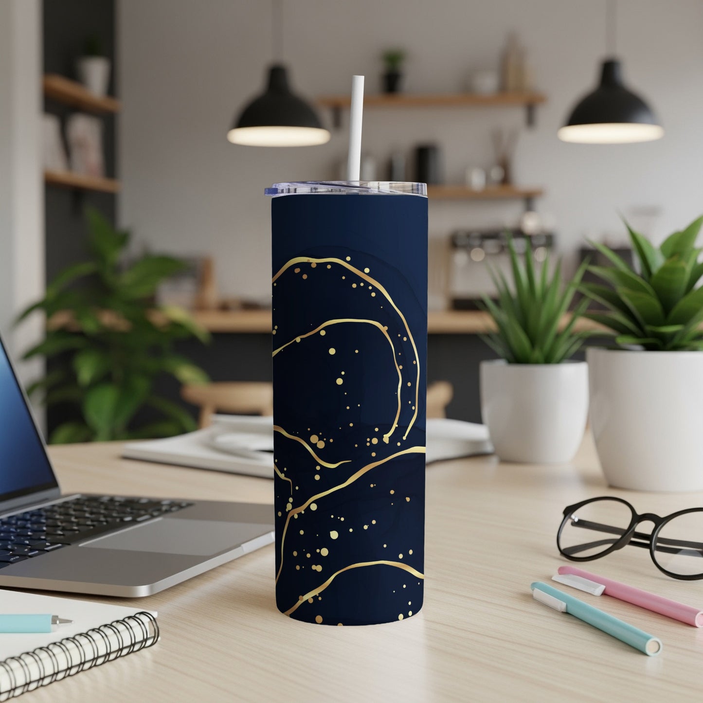 Dark blue tumbler with gold abstract swirls on a desk.