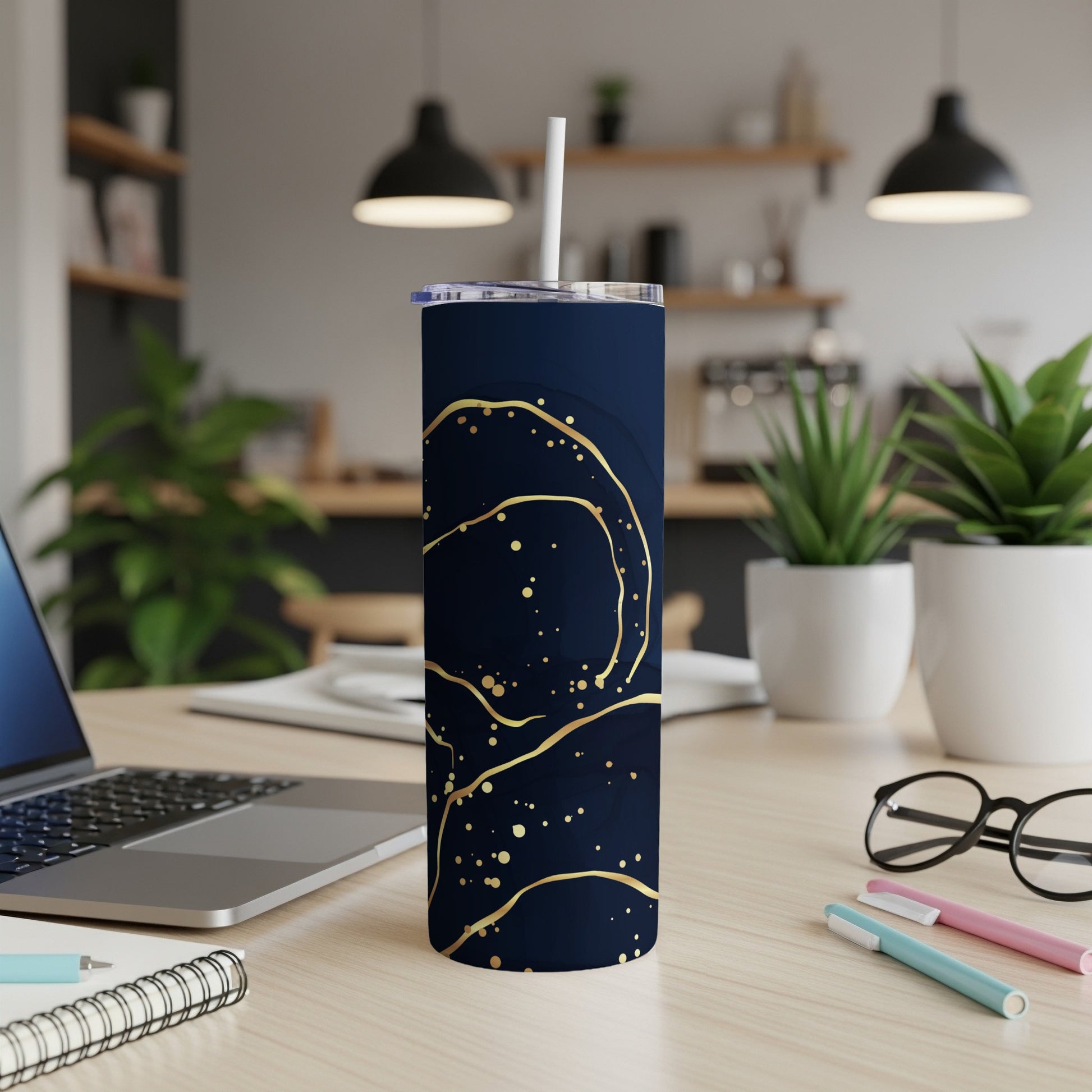 Dark blue tumbler with gold abstract swirls on a desk.