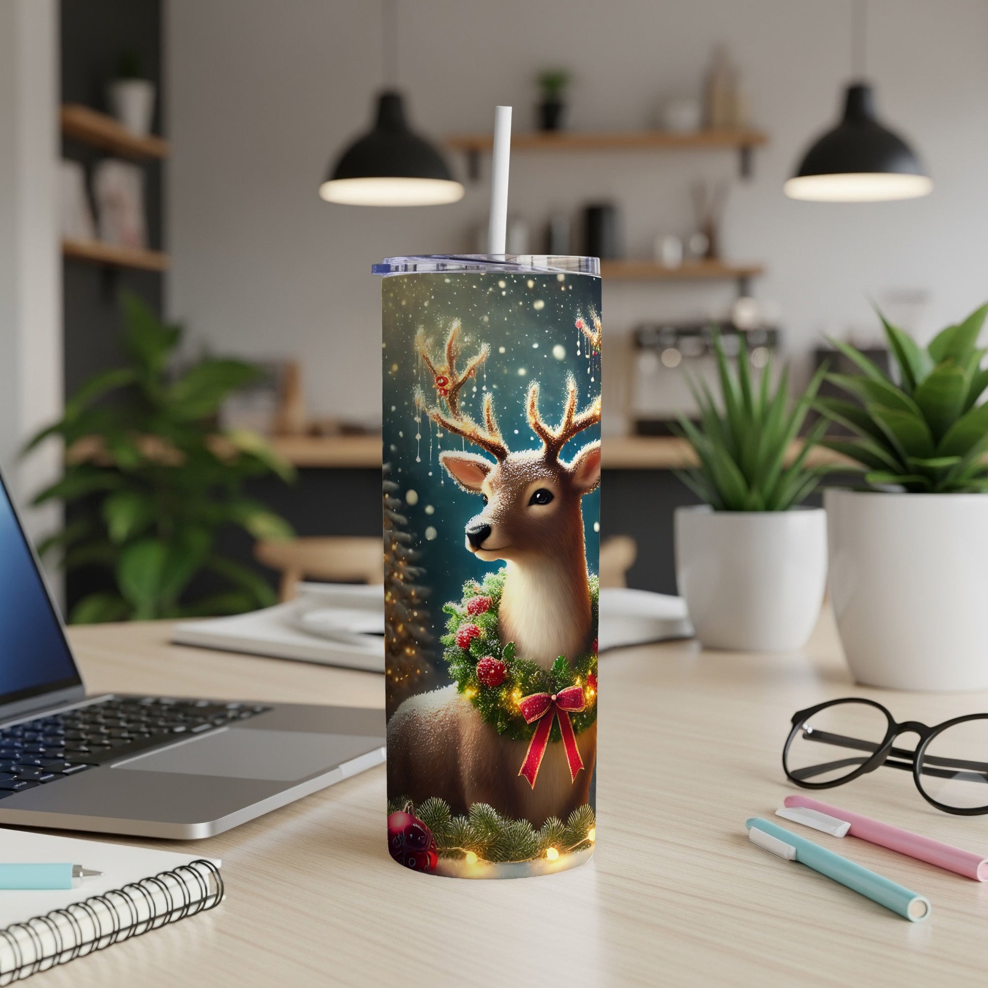 Christmas tumbler with reindeer and festive wreath, next to a laptop.