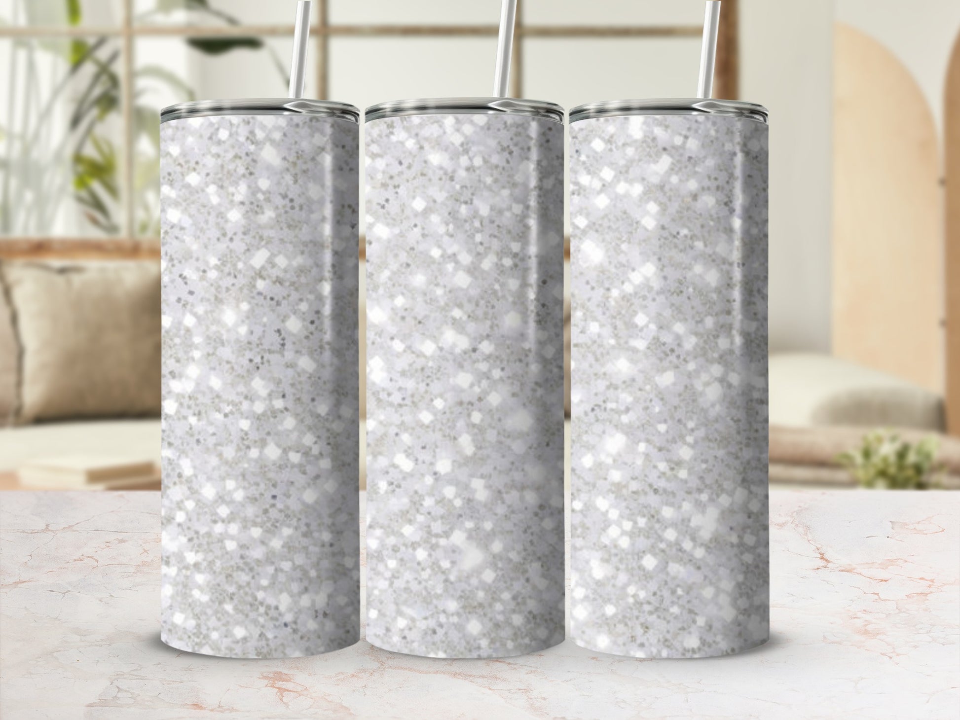 Three speckled glitter tumblers with straws stand on a marble surface.