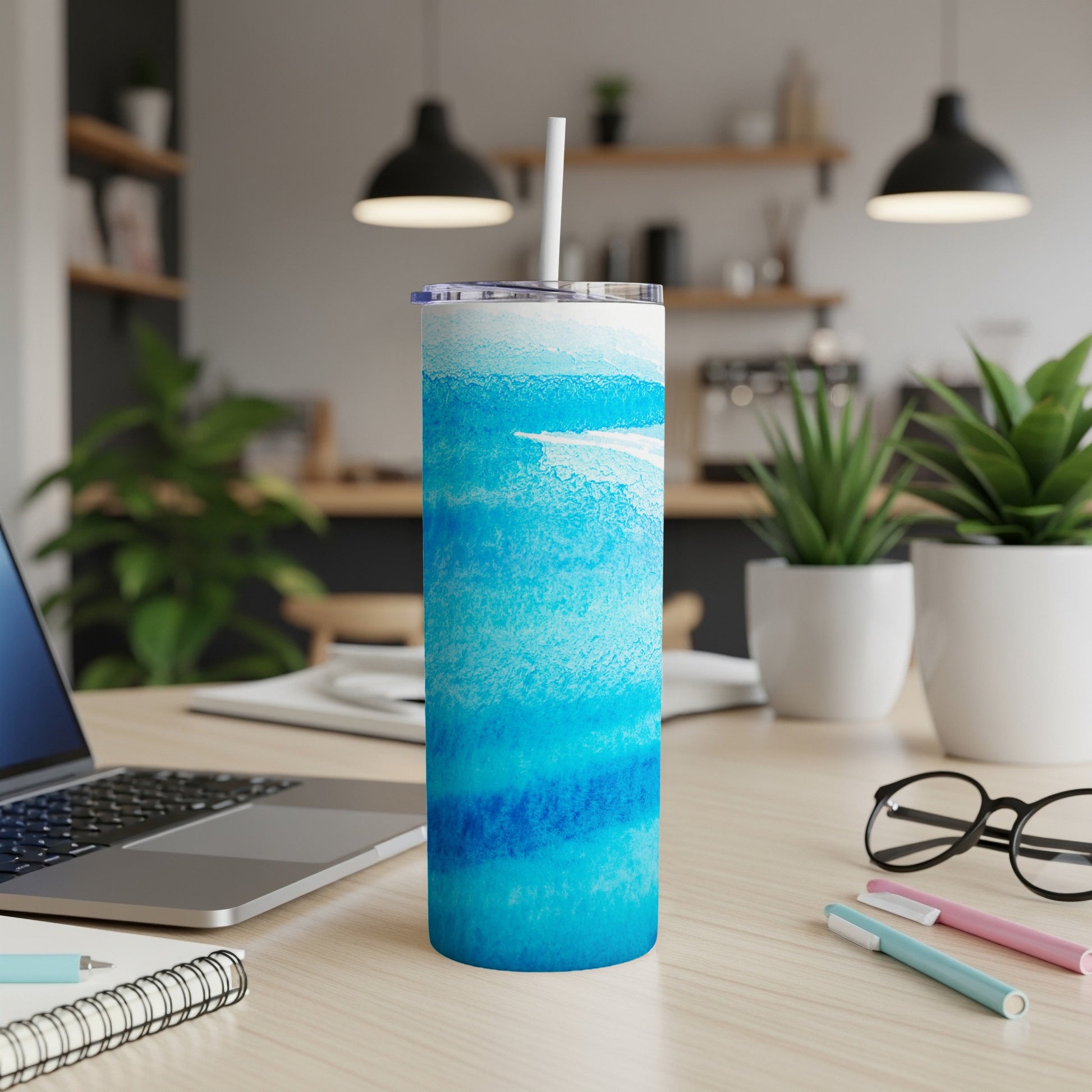 Blue watercolor tumbler with white straw on desk, laptop and plants.