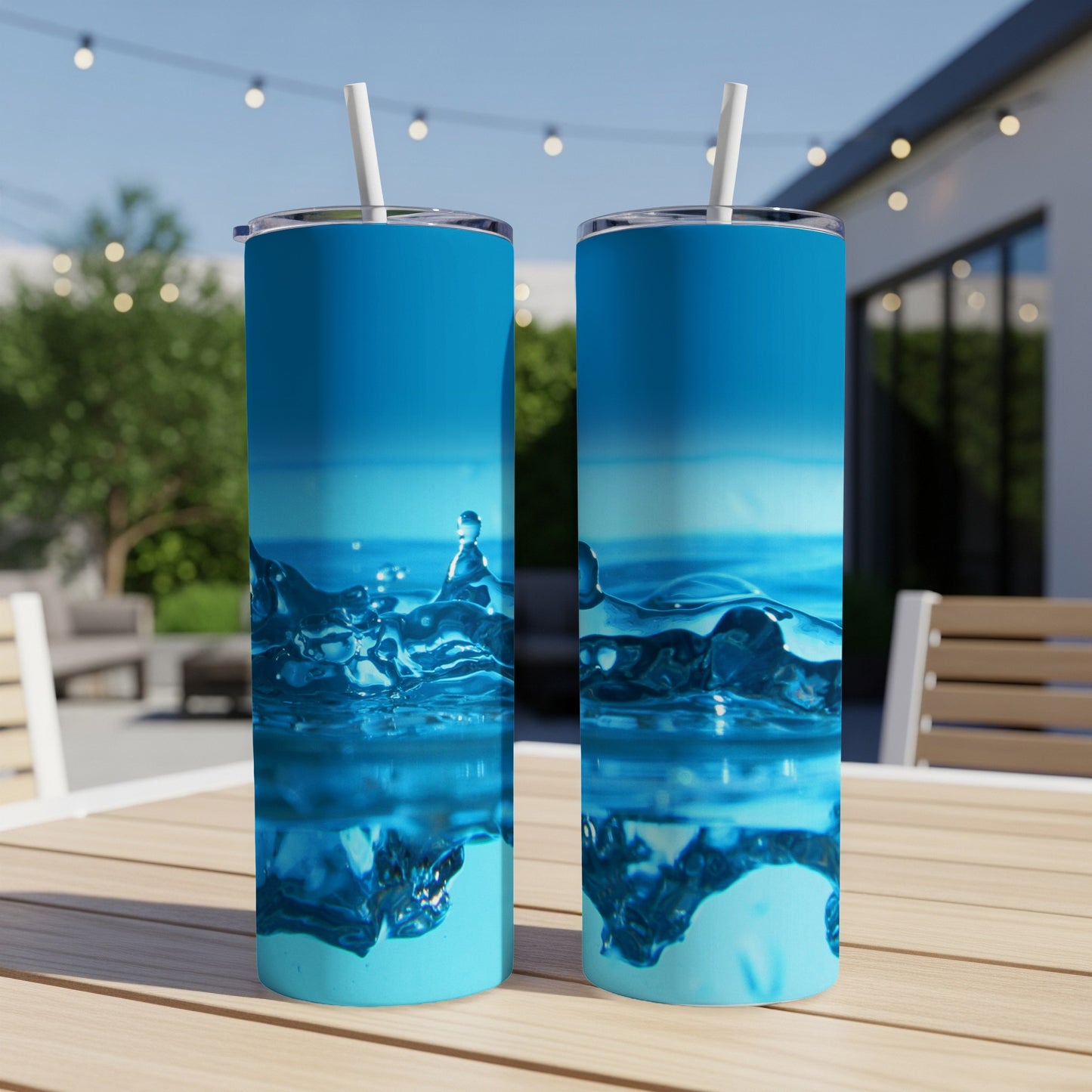 Two blue tumblers with water splash design sit on a wooden table outdoors.