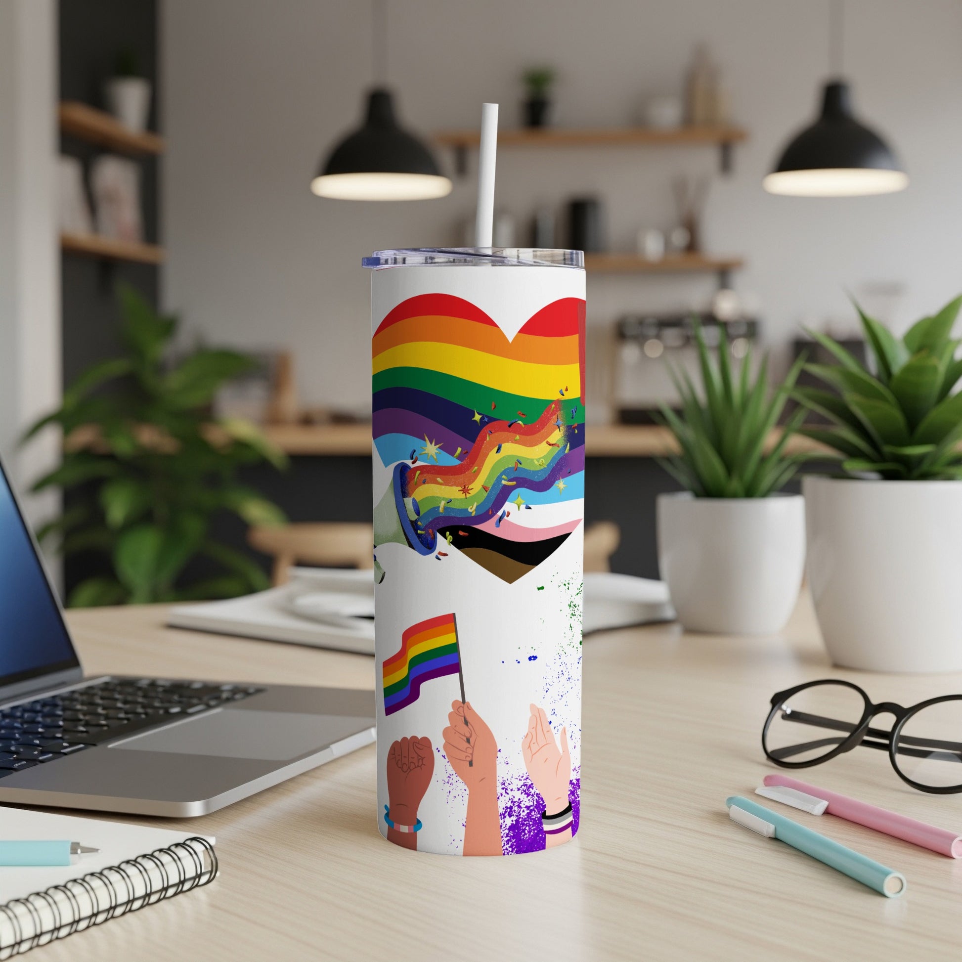 Rainbow pride flag tumbler with diverse hands holding flags, on a desk.