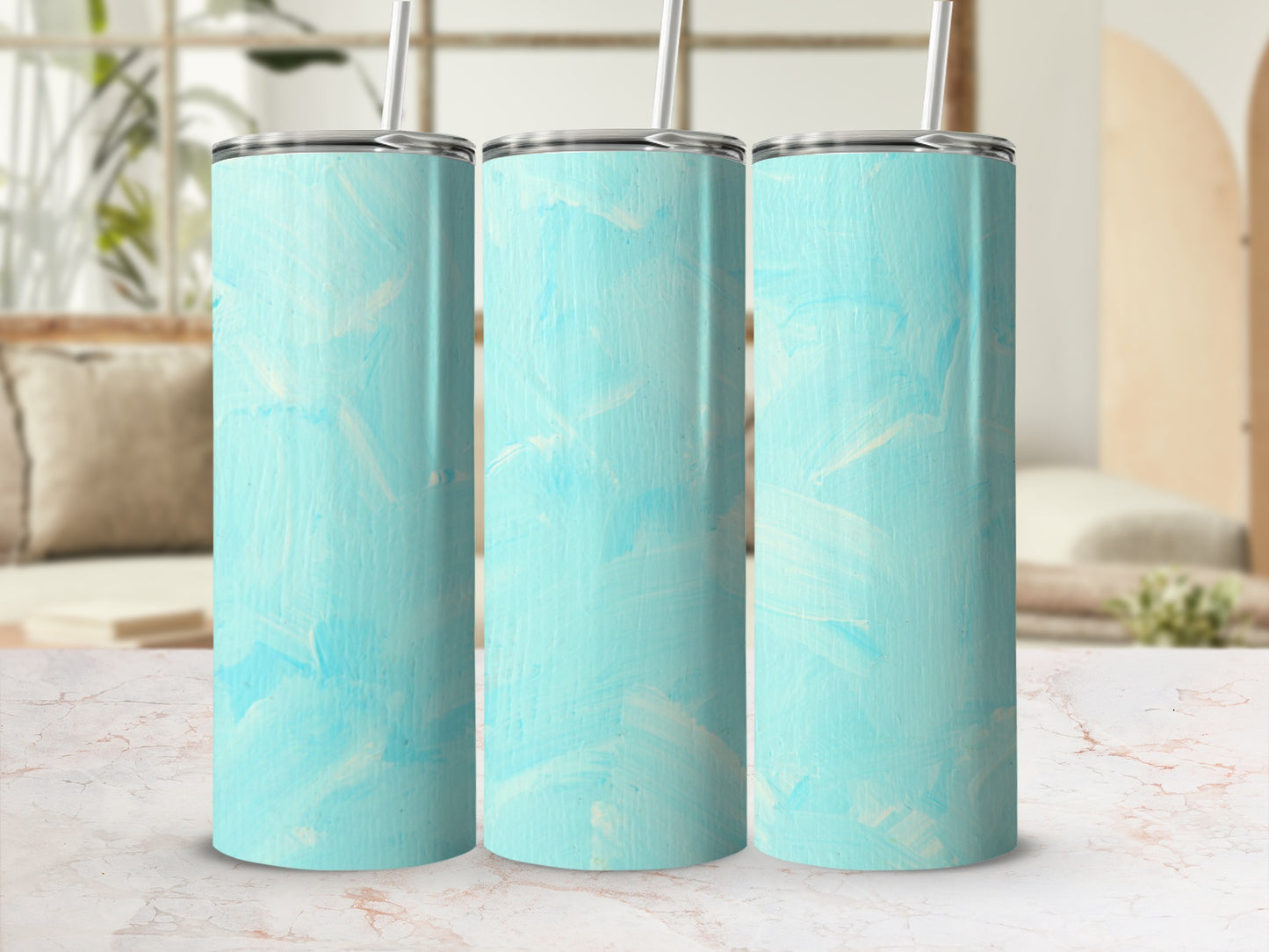 Three light blue painted tumblers with straws on a marble countertop.