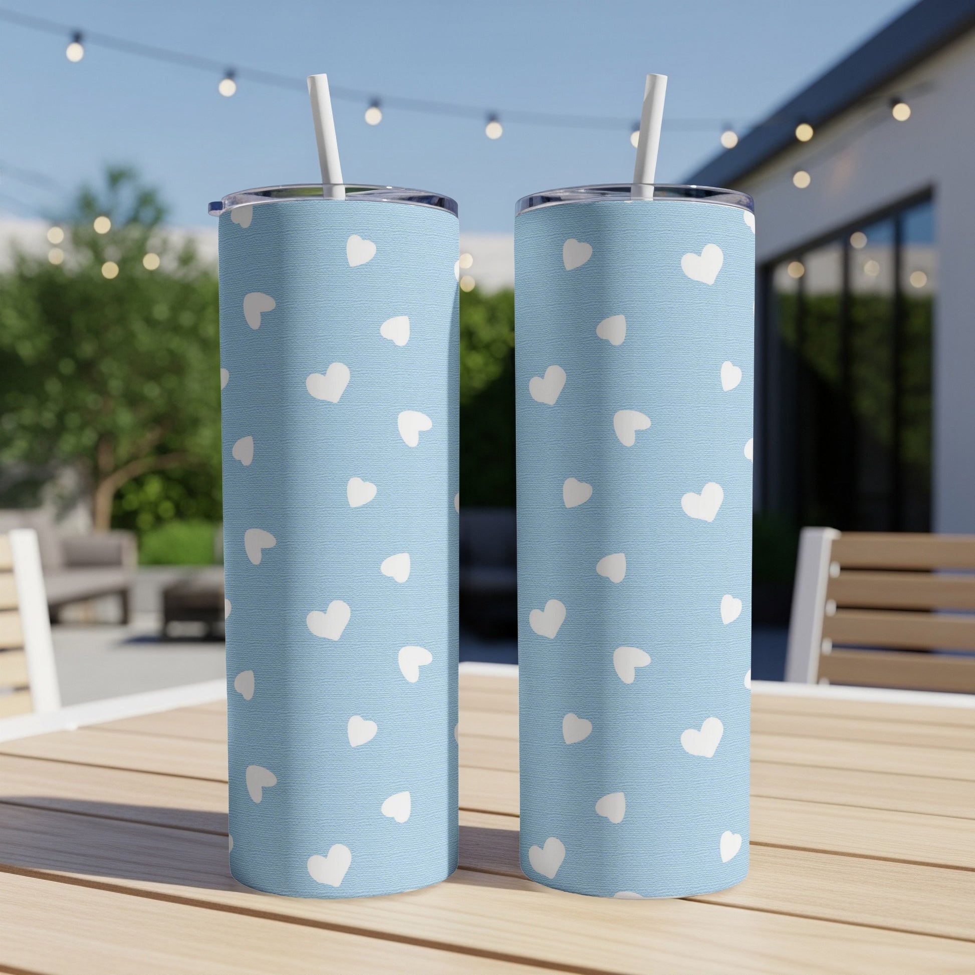 Two blue tumblers with white heart pattern and straws on a wooden table.