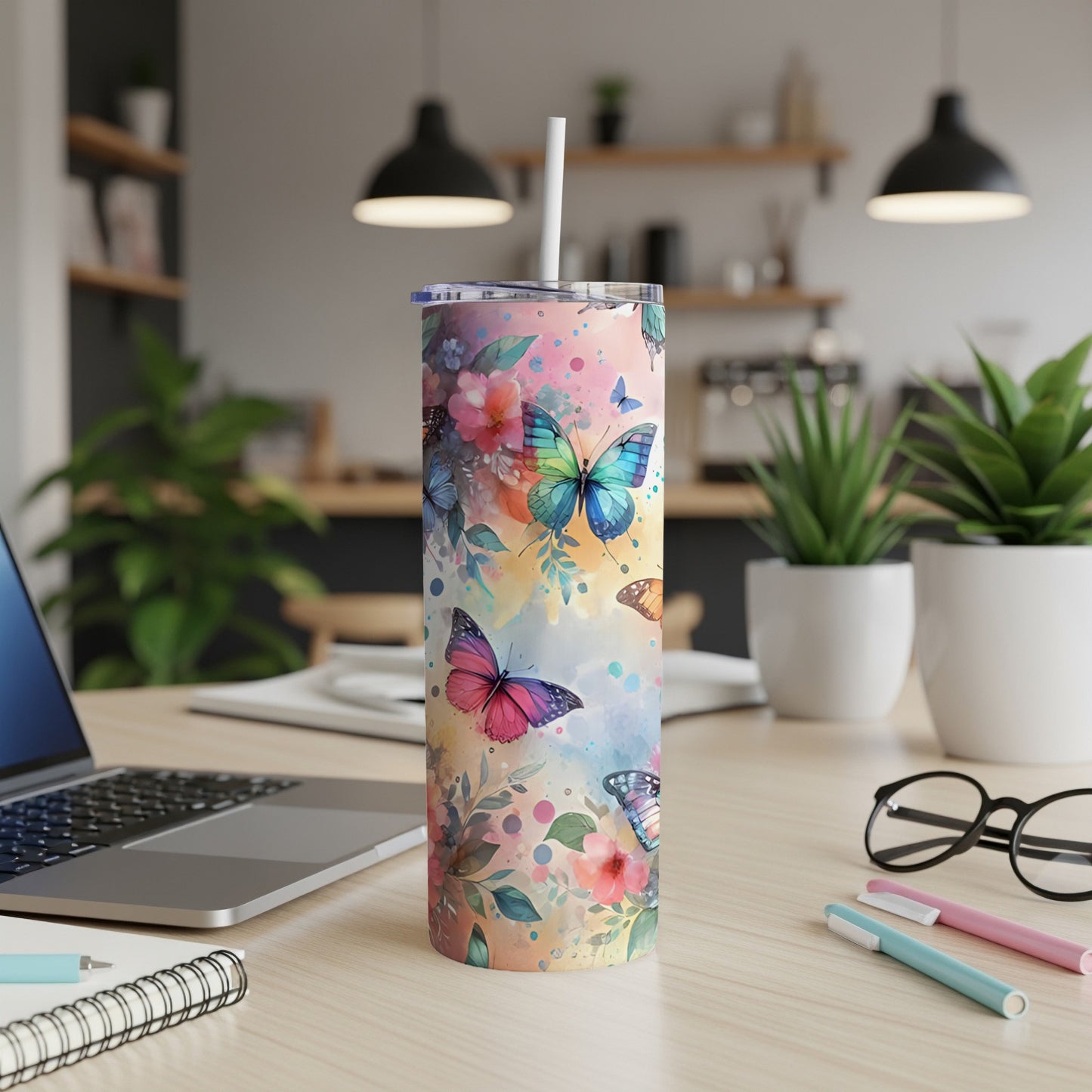 Colorful watercolor butterflies adorn a skinny tumbler with a straw on a desk.