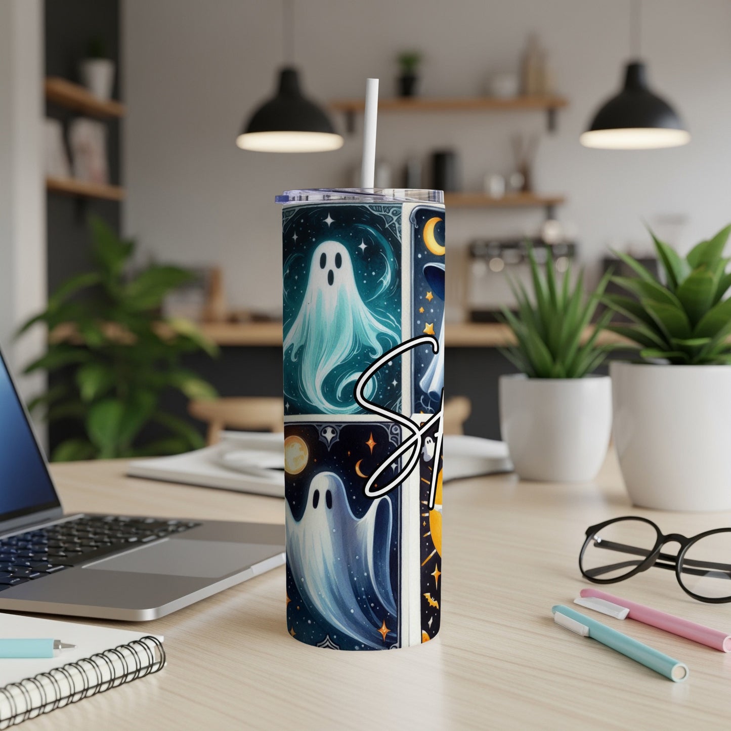 Tumbler with cartoon ghosts, moons, and stars, set on a desk.