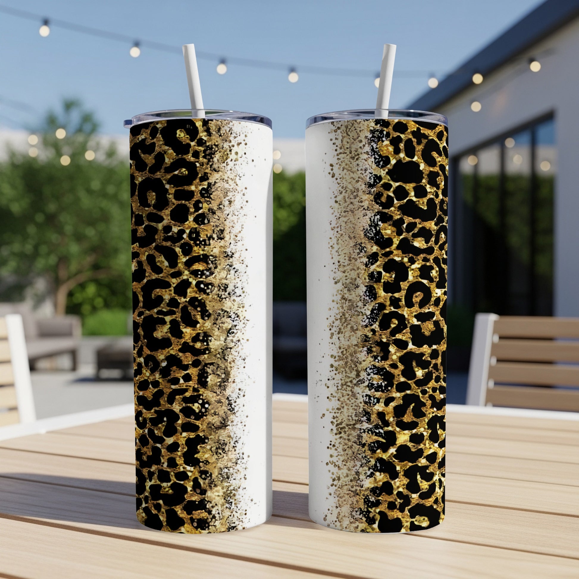 Two leopard print tumblers with straws on a table outdoors.