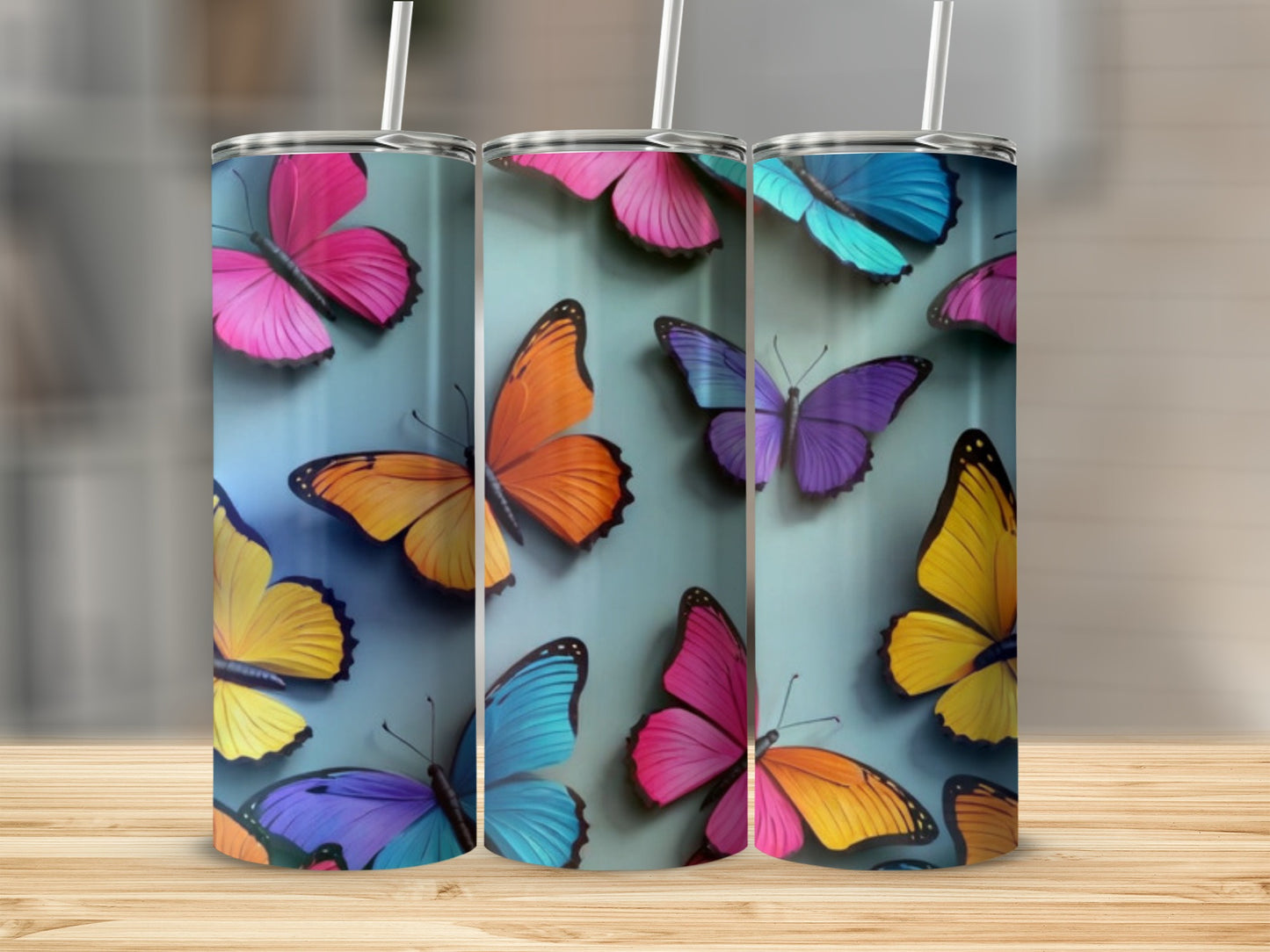 Three tumblers with colorful butterfly designs on a wooden surface.