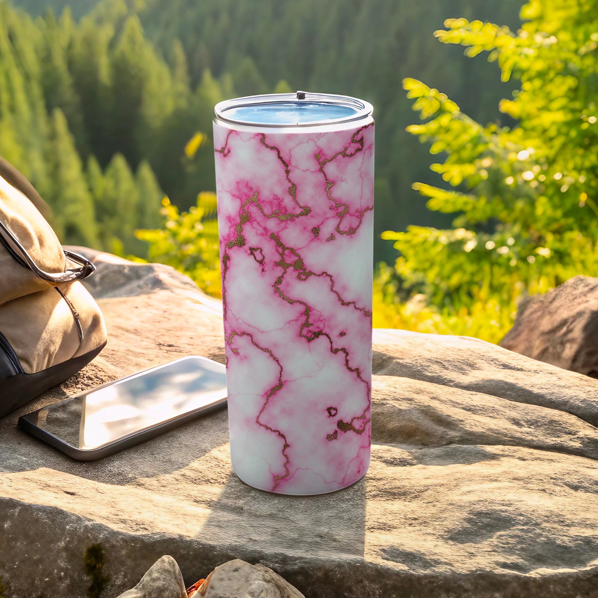 Pink marble tumbler with gold veining, next to a phone on a rock.