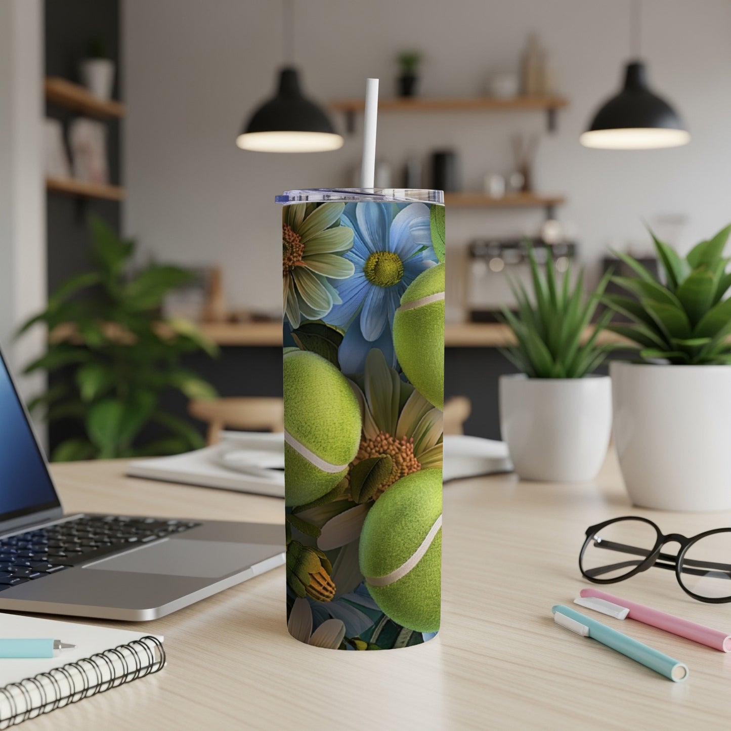 Tumbler with tennis balls and floral design on a desk.