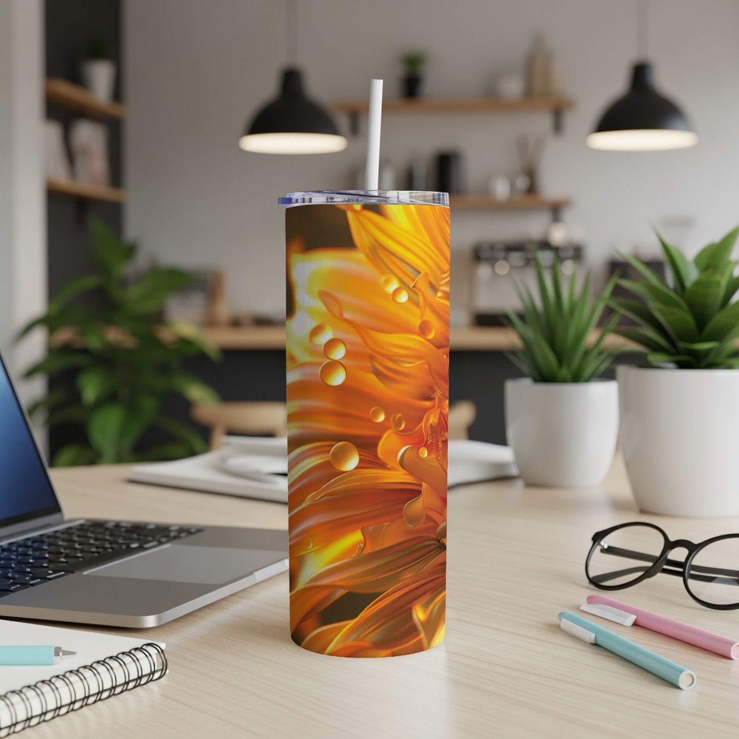 Orange flower with dew drops on a tumbler with laptop and pens.