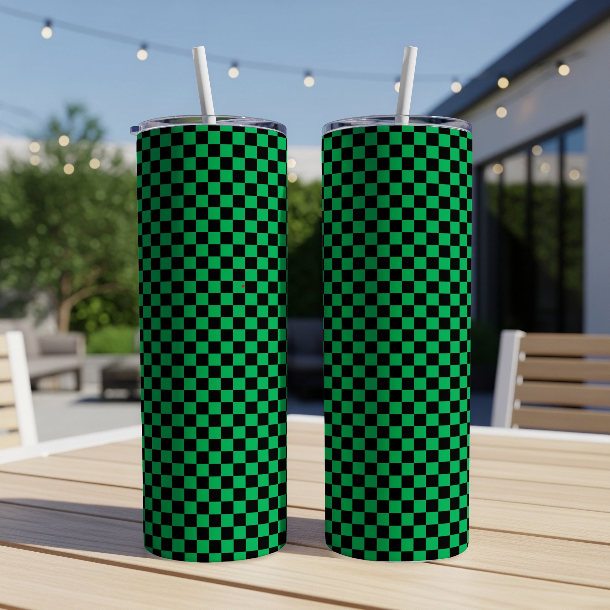 Two green and black checkered tumblers with straws on an outdoor table.